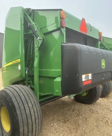Back of a green John Deere agricultural machine with large tires, warning lights, and a black protective cover.