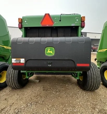Back view of a green John Deere tractor with a black rear cover, large rear tires, and a red triangular slow-moving vehicle sign.