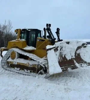 Yellow snowplow clearing snow on a road in a winter landscape.