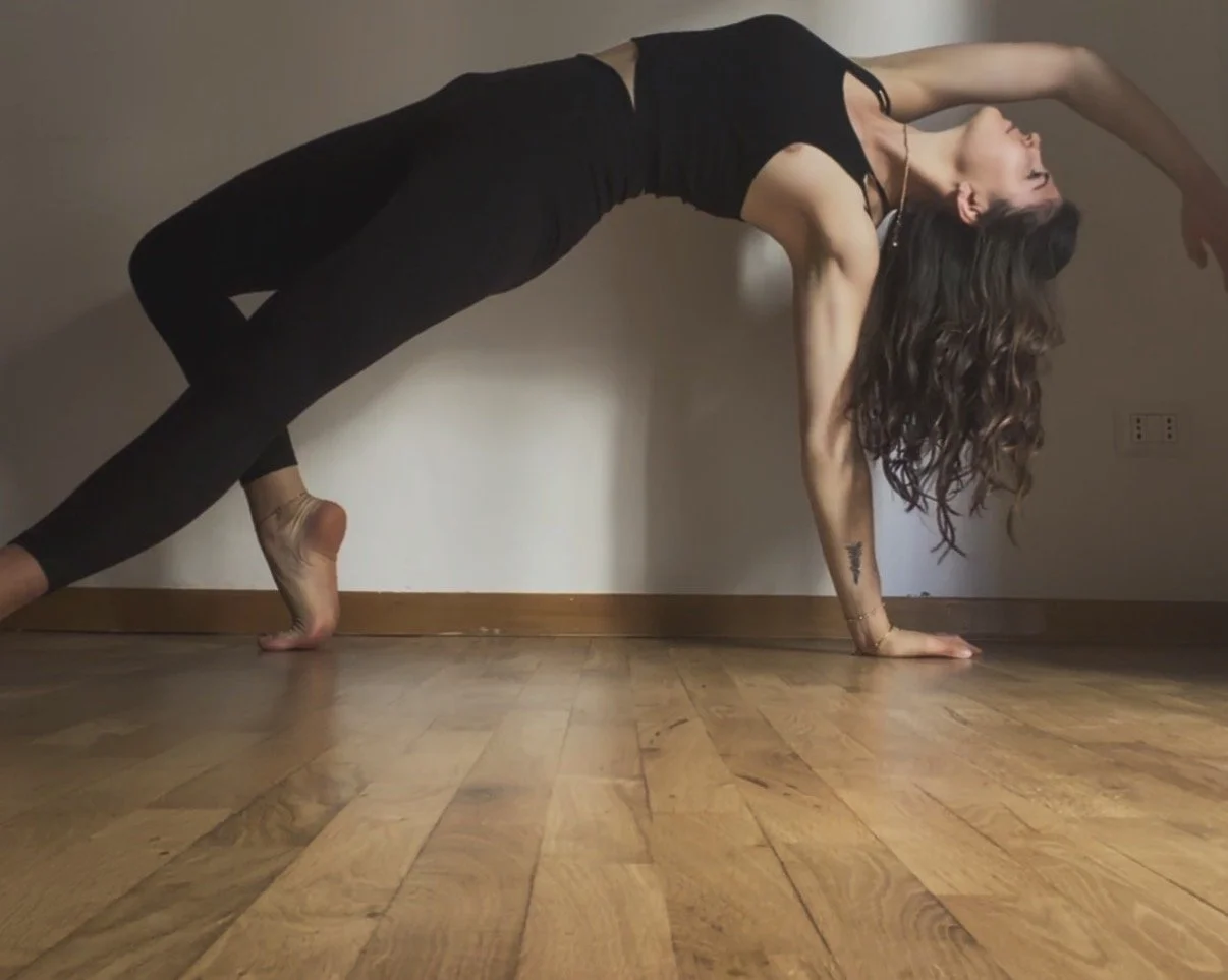 A woman practicing yoga in a bridge pose on a wooden floor inside a room.