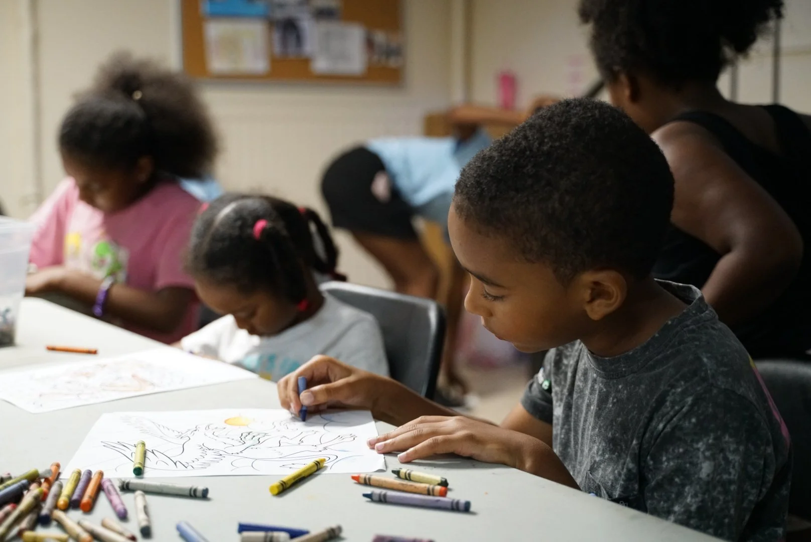 Children sitting at a table coloring with crayons in a classroom.