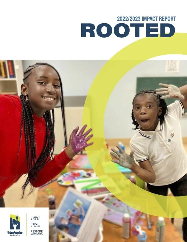 Two young girls engaging in arts and crafts activities in a classroom, smiling and with painted hands, on the cover of the 2022/2023 impact report for Roots, an organization in Toronto.