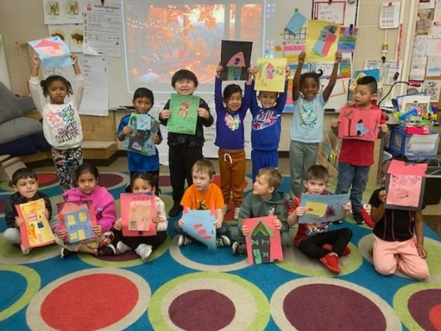 Group of young children in a classroom showing their colorful paper house art projects.