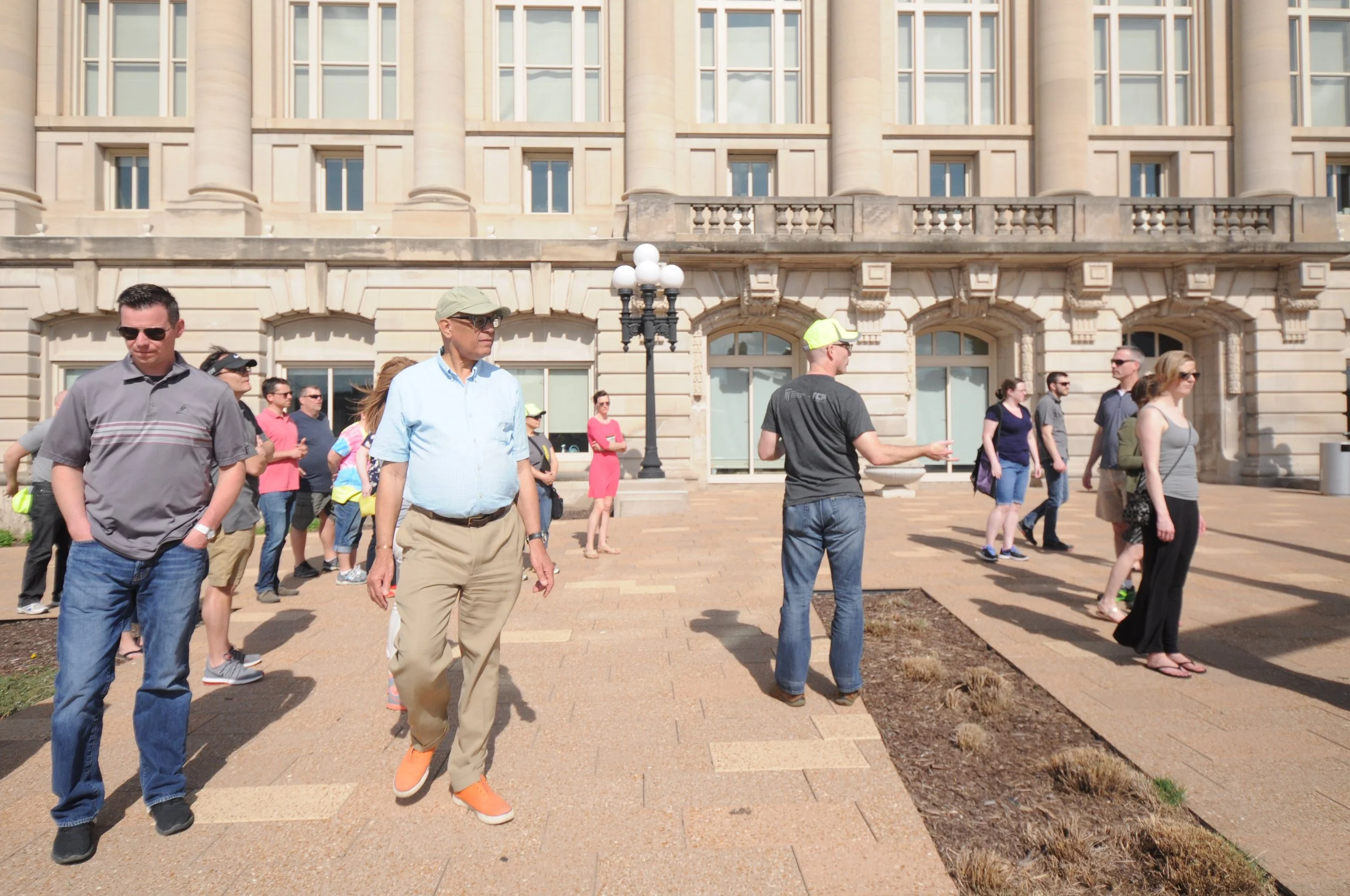 A group of people standing outside a large classical-style building with columns and arched windows.