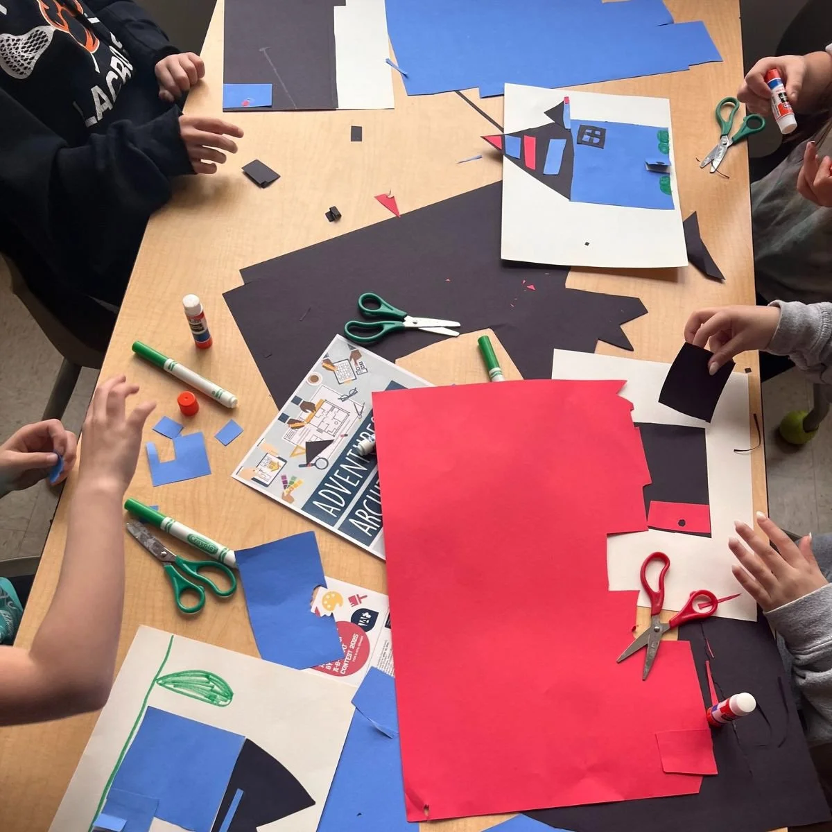 Children working on a paper craft project involving cutting, gluing, and assembling colored paper to create a picture of a house.