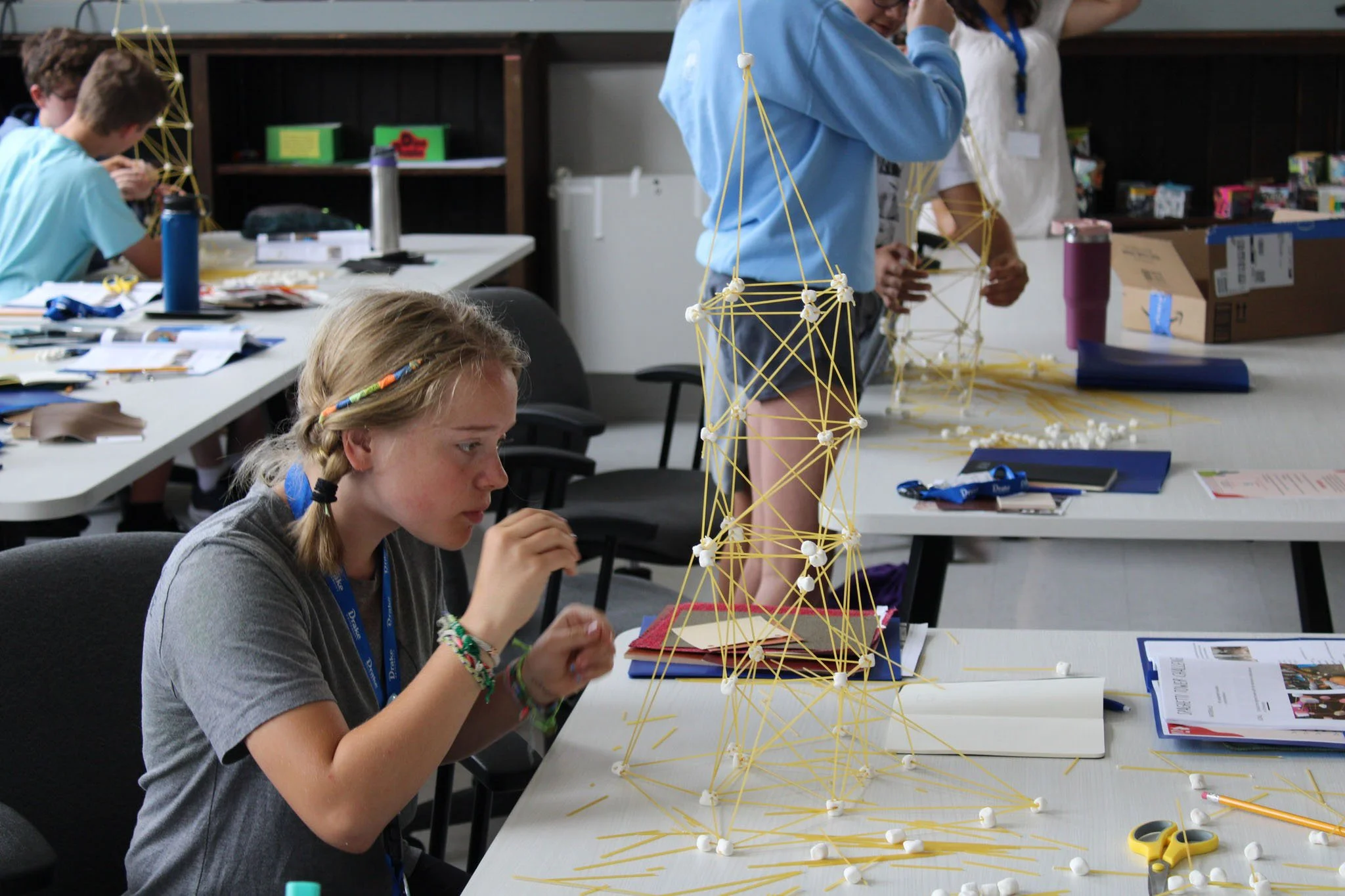 Young girl with braided hair building a sculpture with spaghetti and marshmallows in a classroom activity.