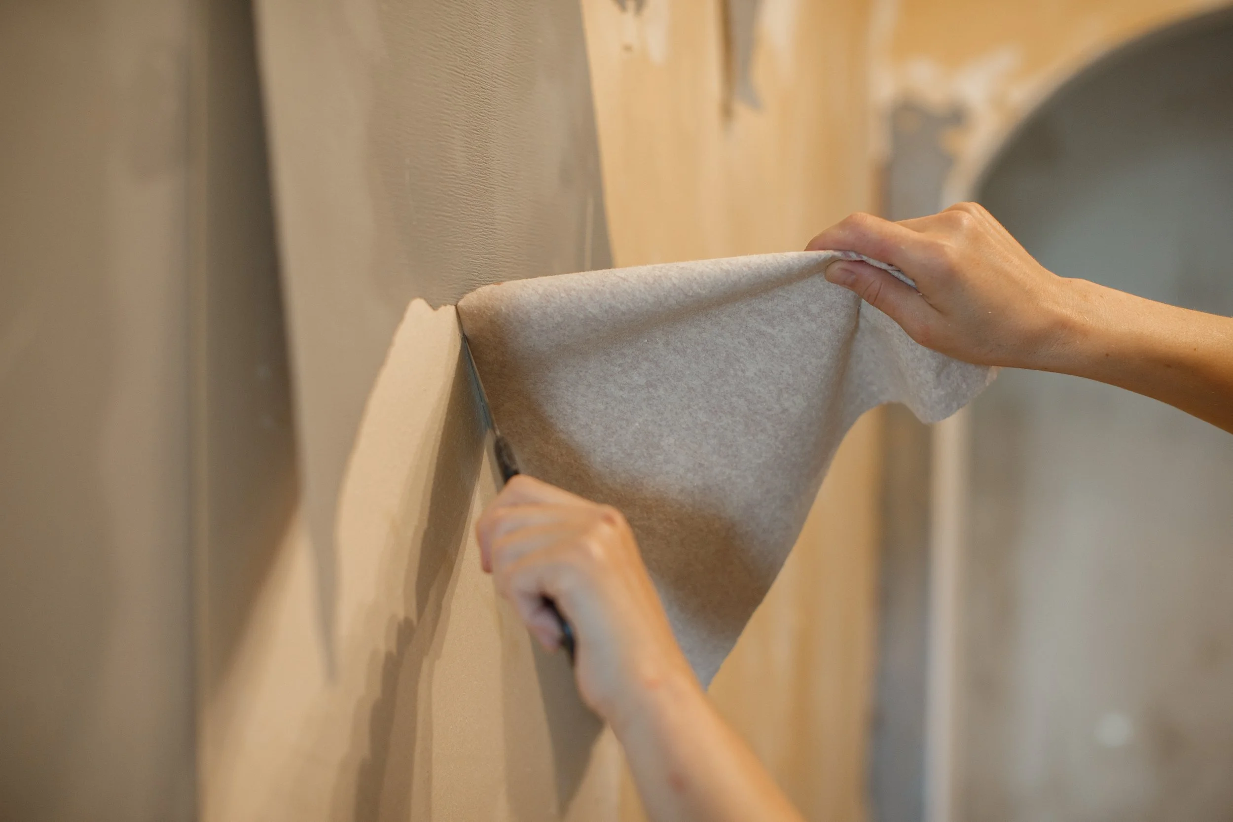 A person peeling wallpaper off a wall.