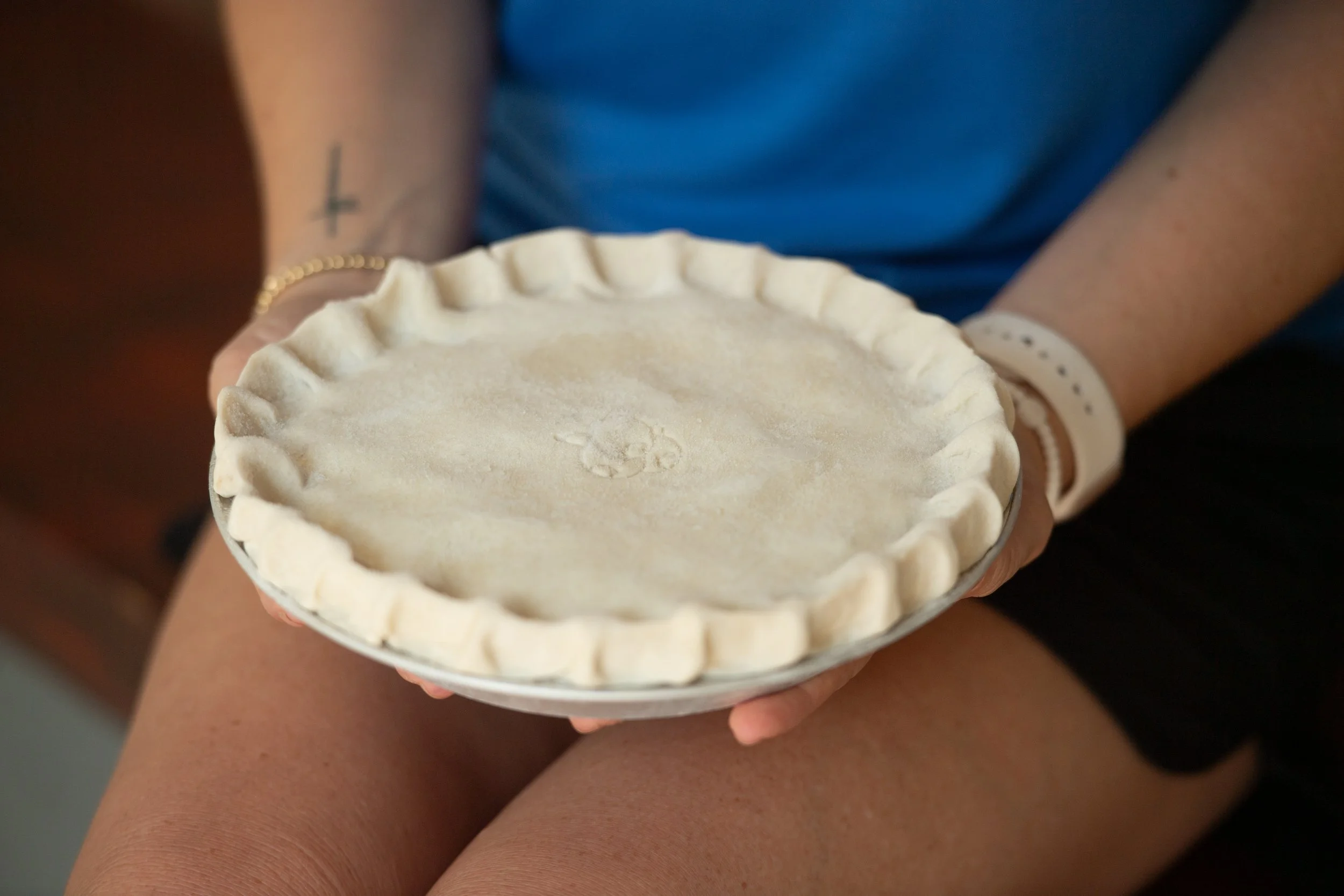 Person holding an unbaked pie crust in a decorative pie dish.