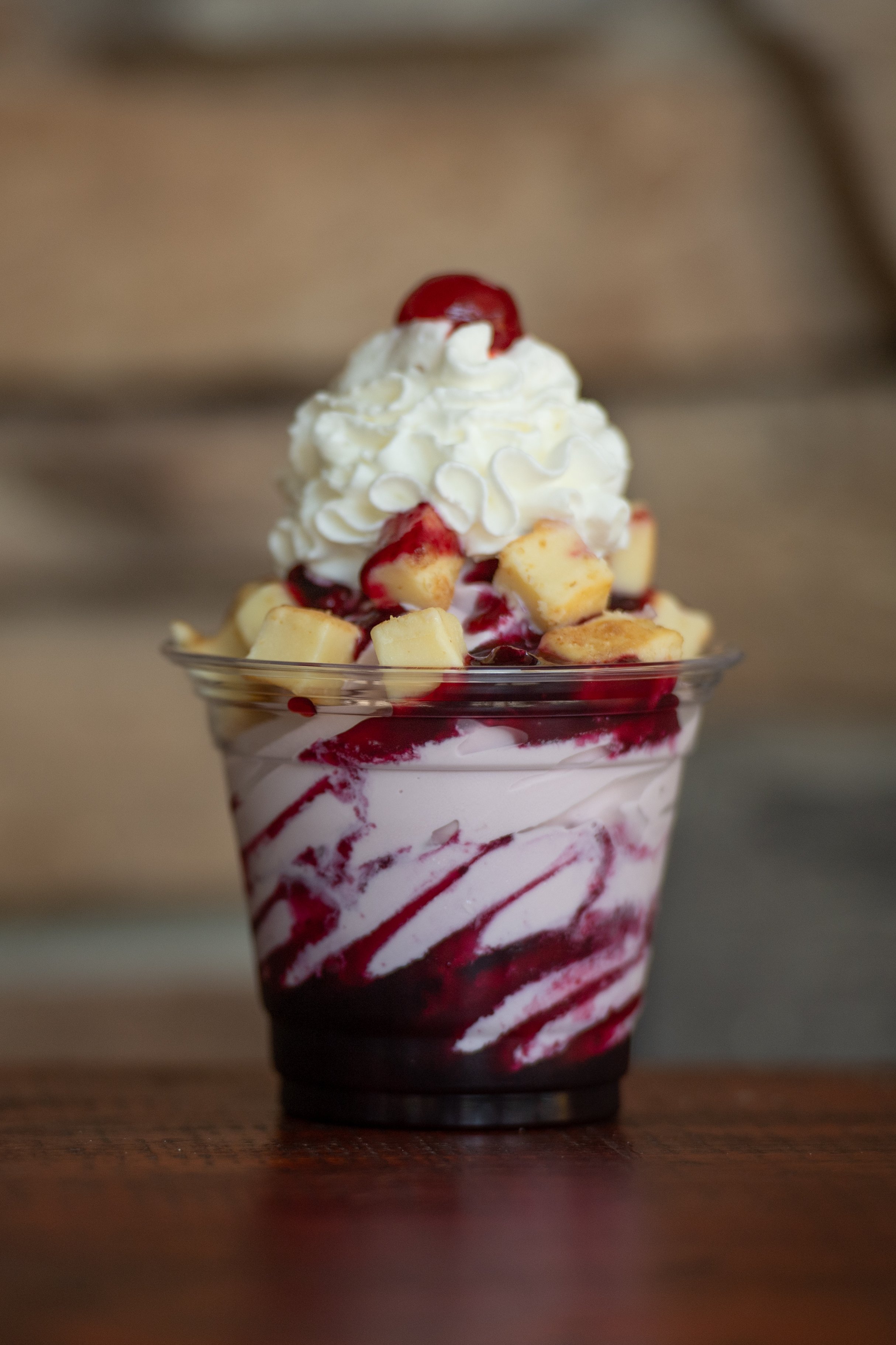 Ice cream sundae with whipped cream, cherries, white chocolate chunks, and berry sauce in a clear plastic cup.