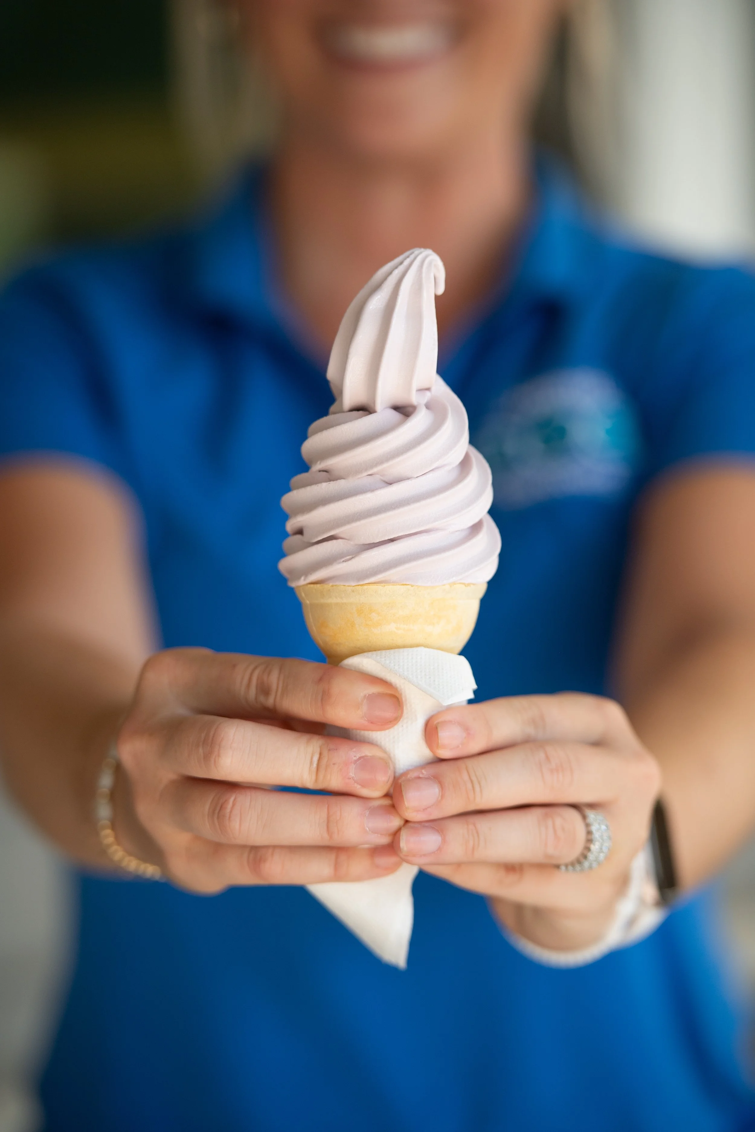 Person in a blue shirt holding a soft-serve ice cream cone with light purple and white swirled ice cream.