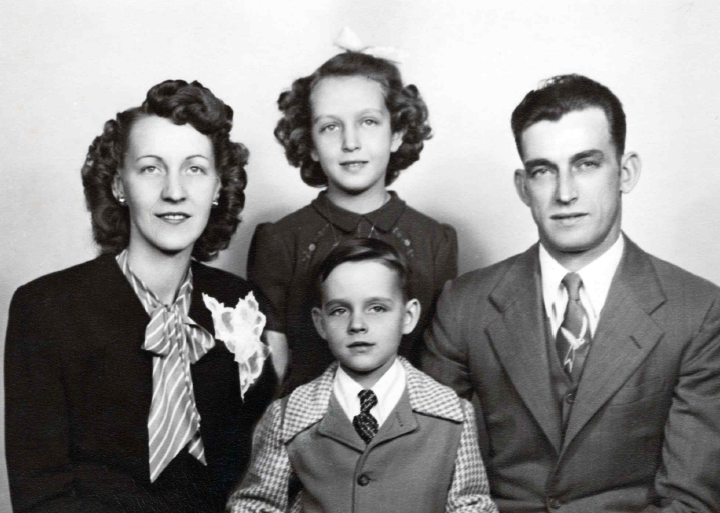 Black and white photograph of a family of four, two women and two children, dressed in vintage clothing, posing for a portrait.
