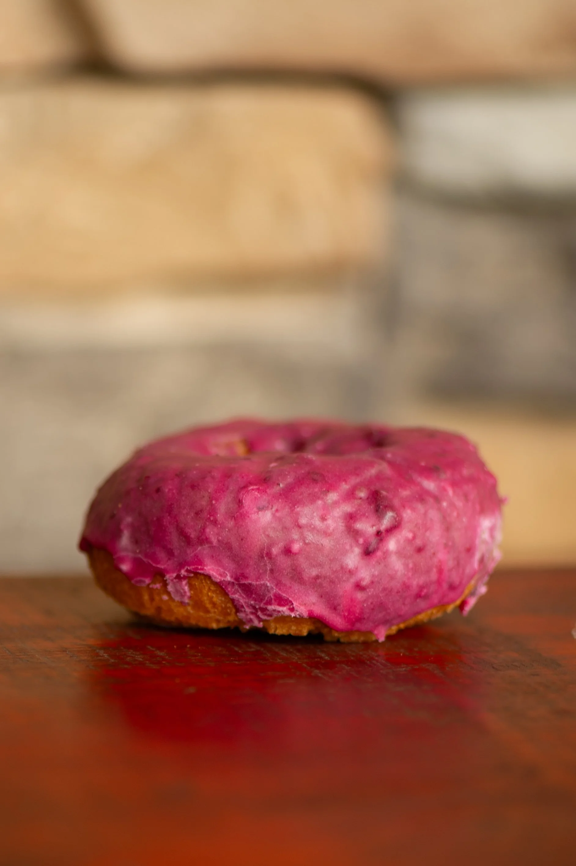 A pink frosted donut with a textured surface on a wooden surface.