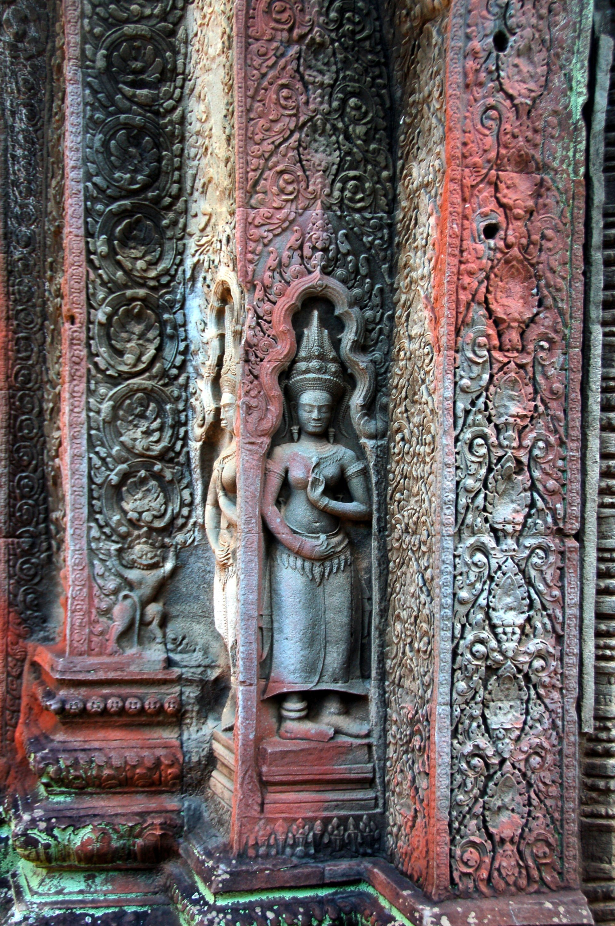 Carved stone sculpture of a female figure with snake in hand, set in an ornate, decorated frame on an ancient temple wall in Cambodia.