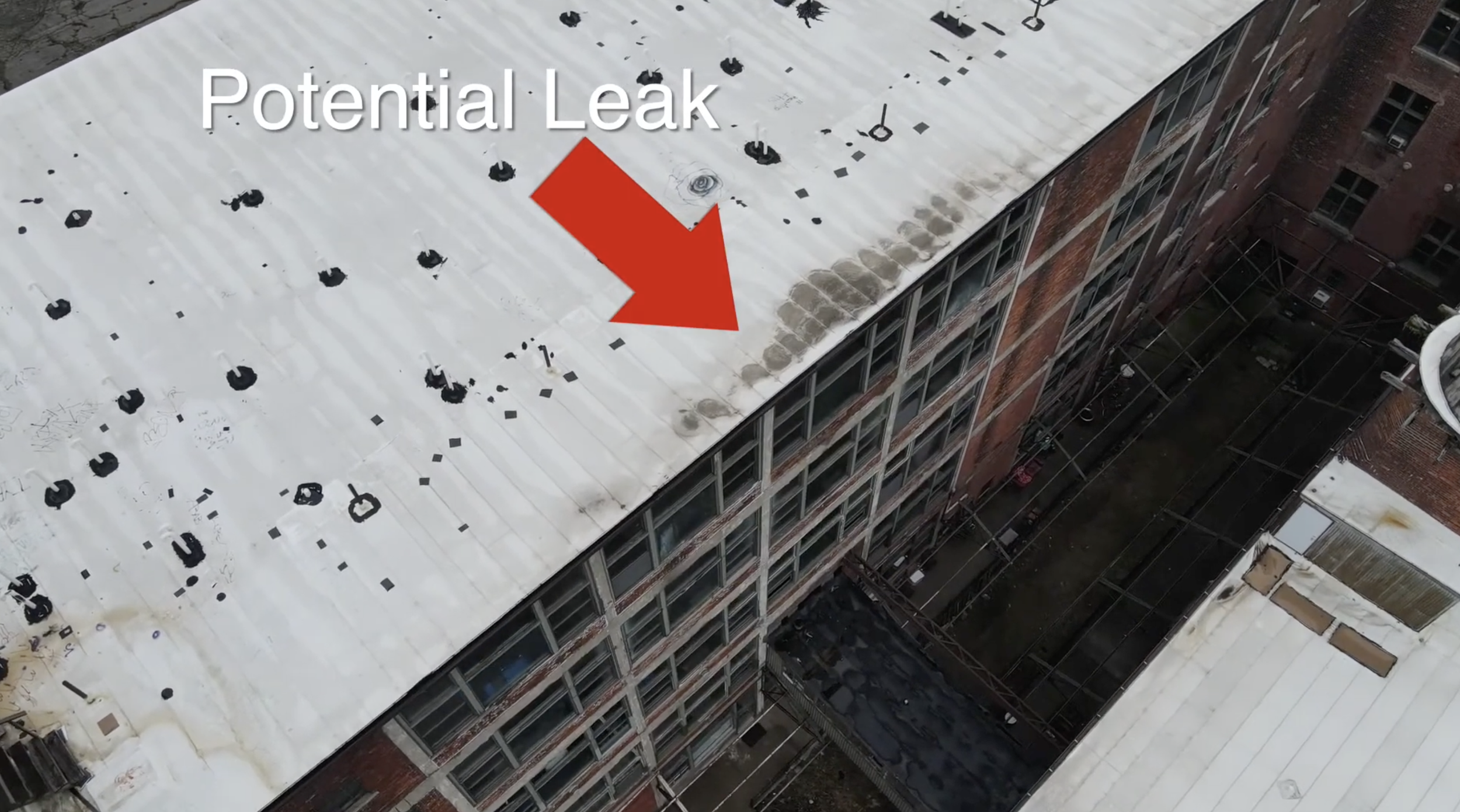 Aerial view of a rooftop with potential leak indicated by a red arrow, showing dark stains and damage on the white surface.
