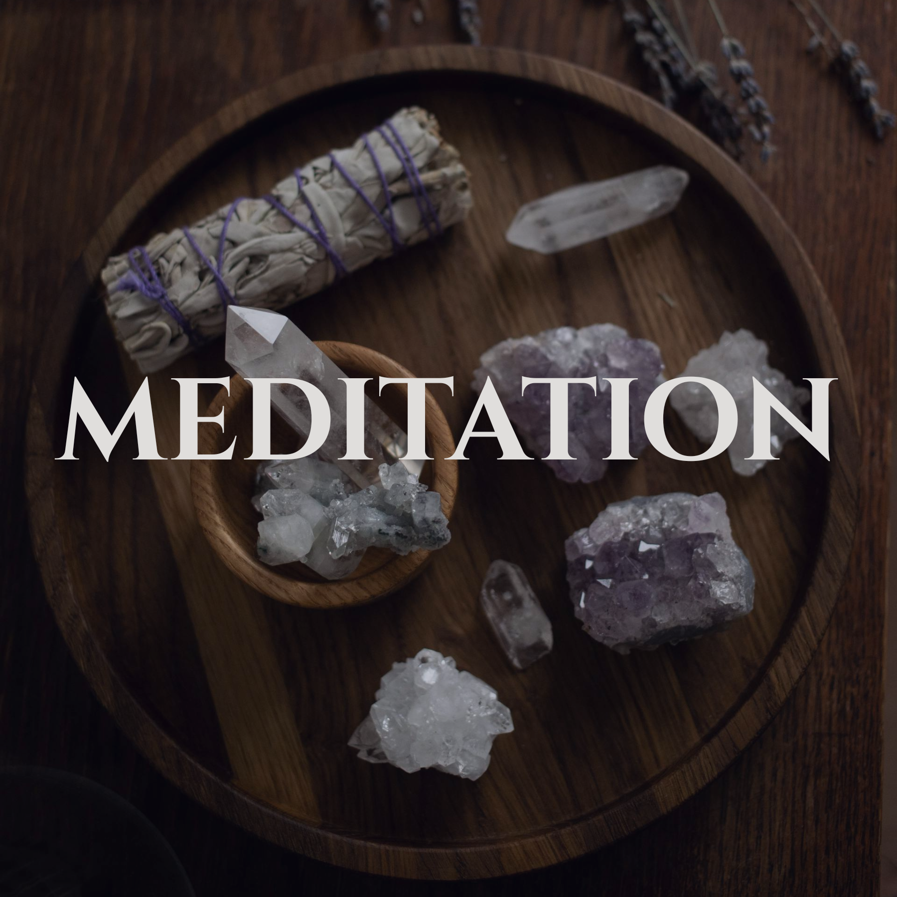 Various crystals and a sage bundle tied with purple string on a wooden circular tray, with dried lavender in the background, representing a meditation setup.