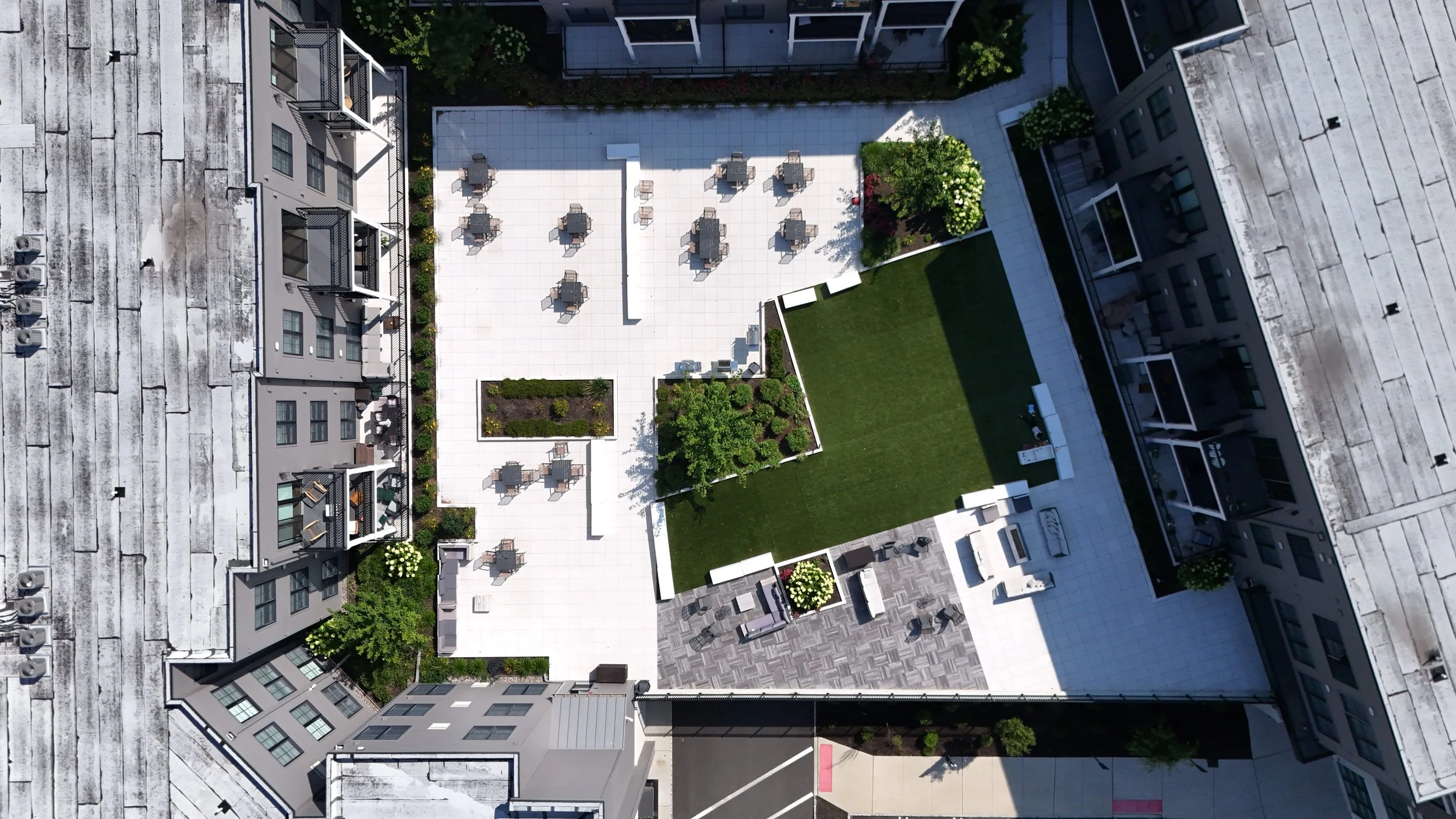 An aerial view of a modern apartment complex's courtyard showing a mixture of outdoor seating, a grassy area, and landscaped flower beds.