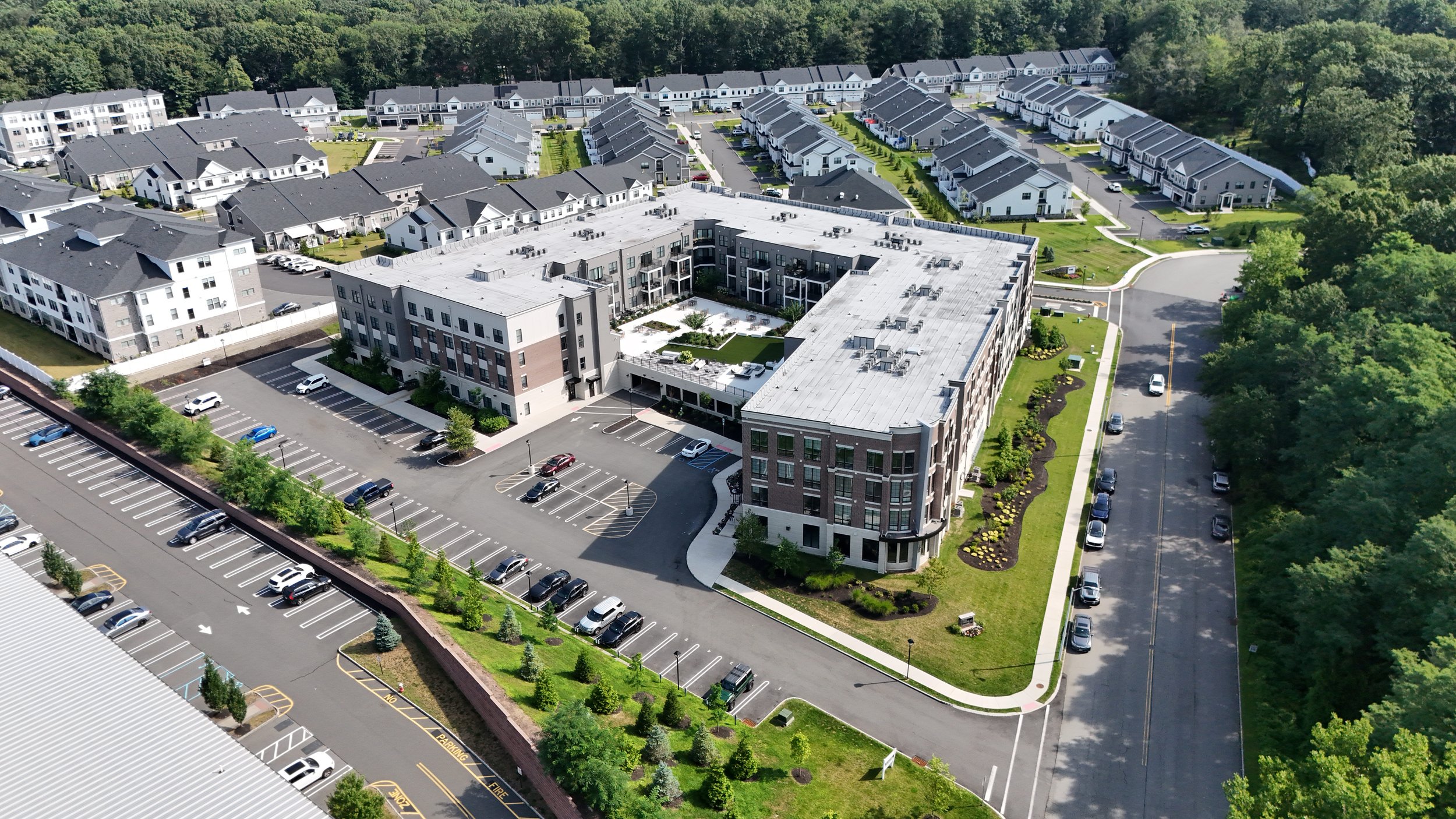 Aerial view of a modern apartment complex with surrounding parking lots, townhouses, and greenery.