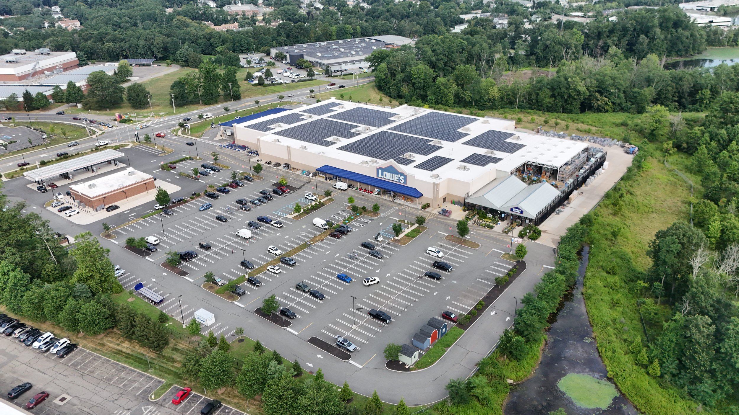 Aerial view of a Lowe's home improvement store with a large parking lot, surrounded by trees and a small creek.