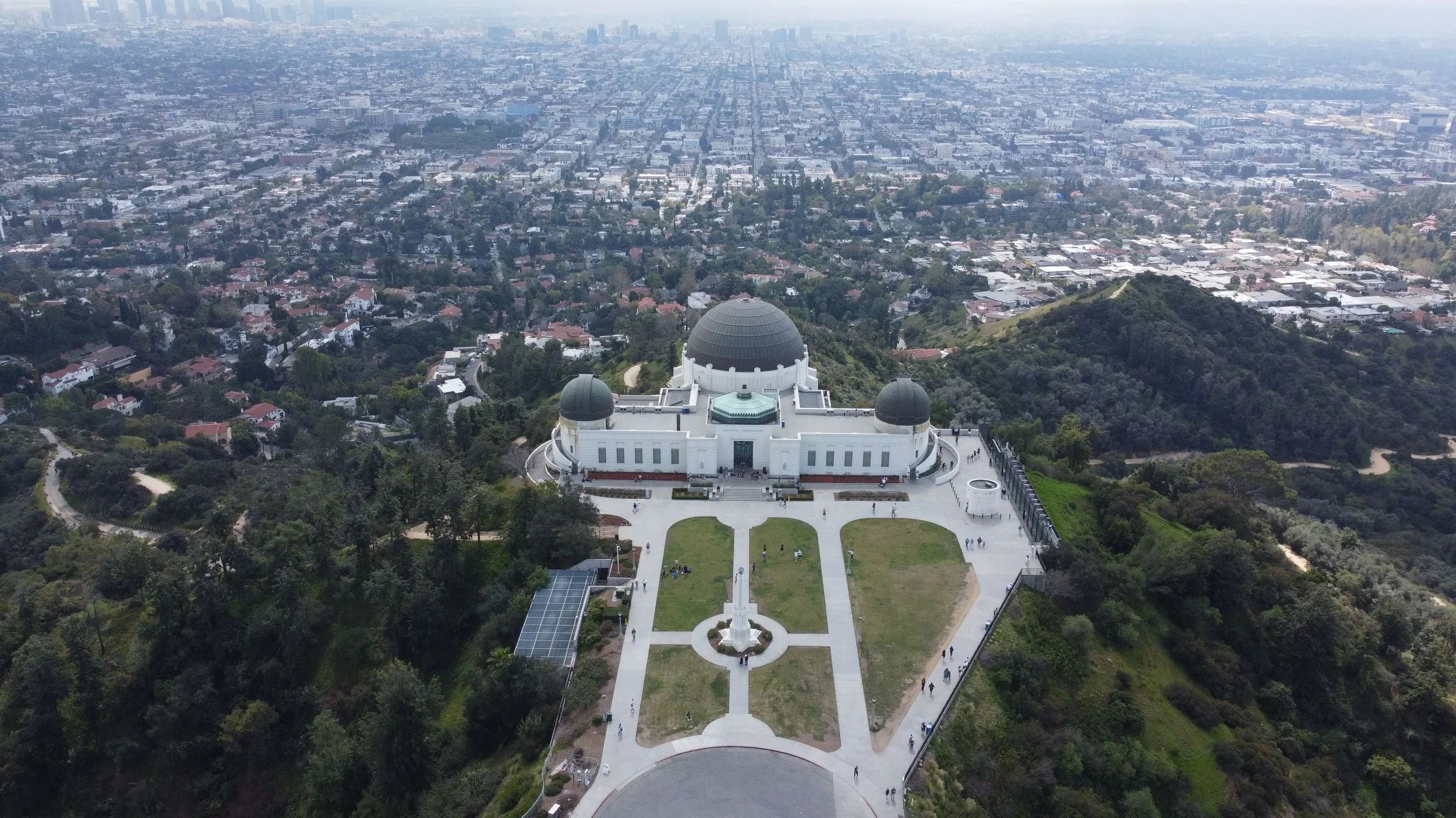 Aerial view of the Griffith Observatory atop a hill with a cityscape extending into the distance.