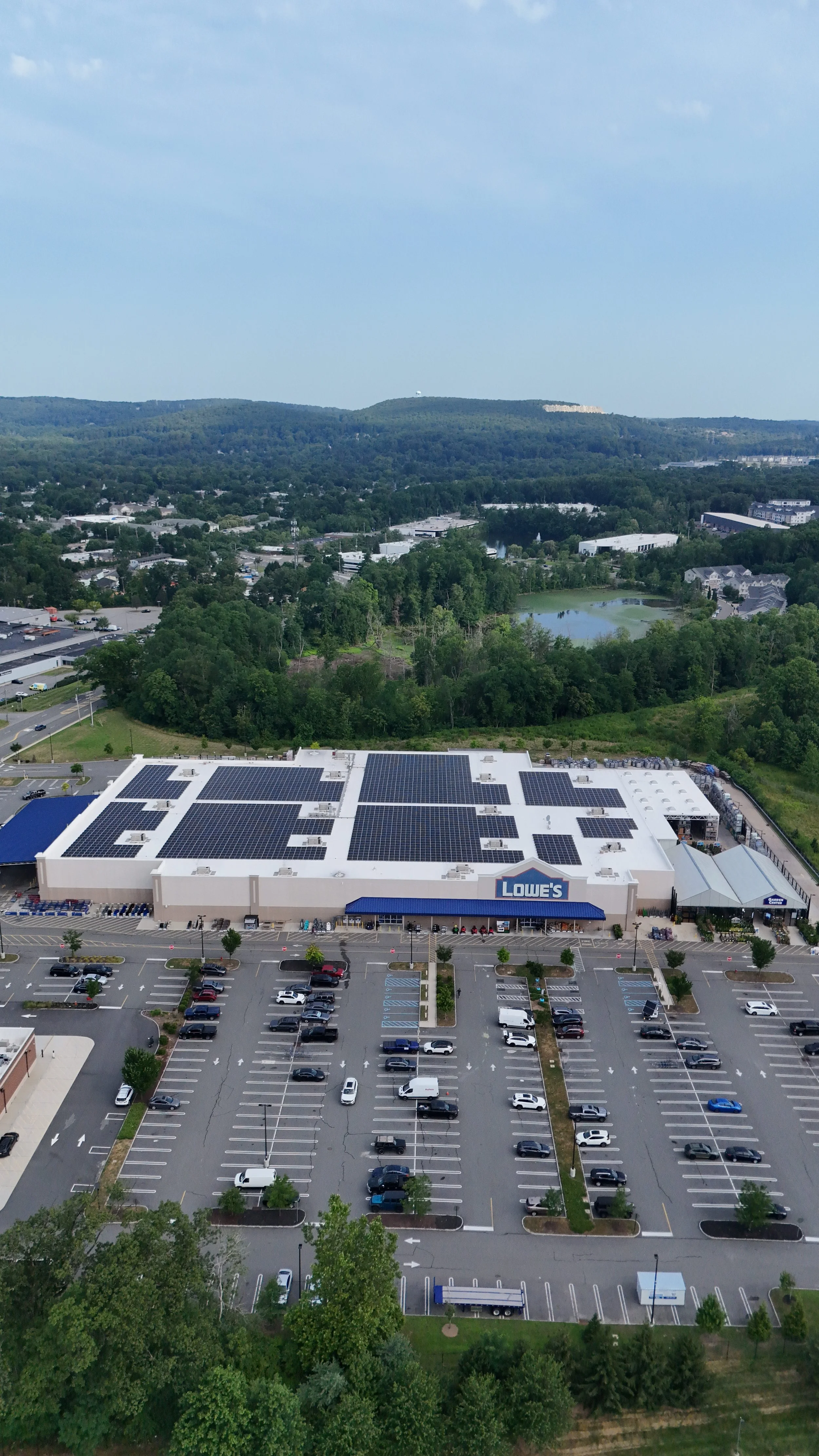 Aerial view of a Lowe's store with solar panels on the roof, surrounded by parking lot and greenery.