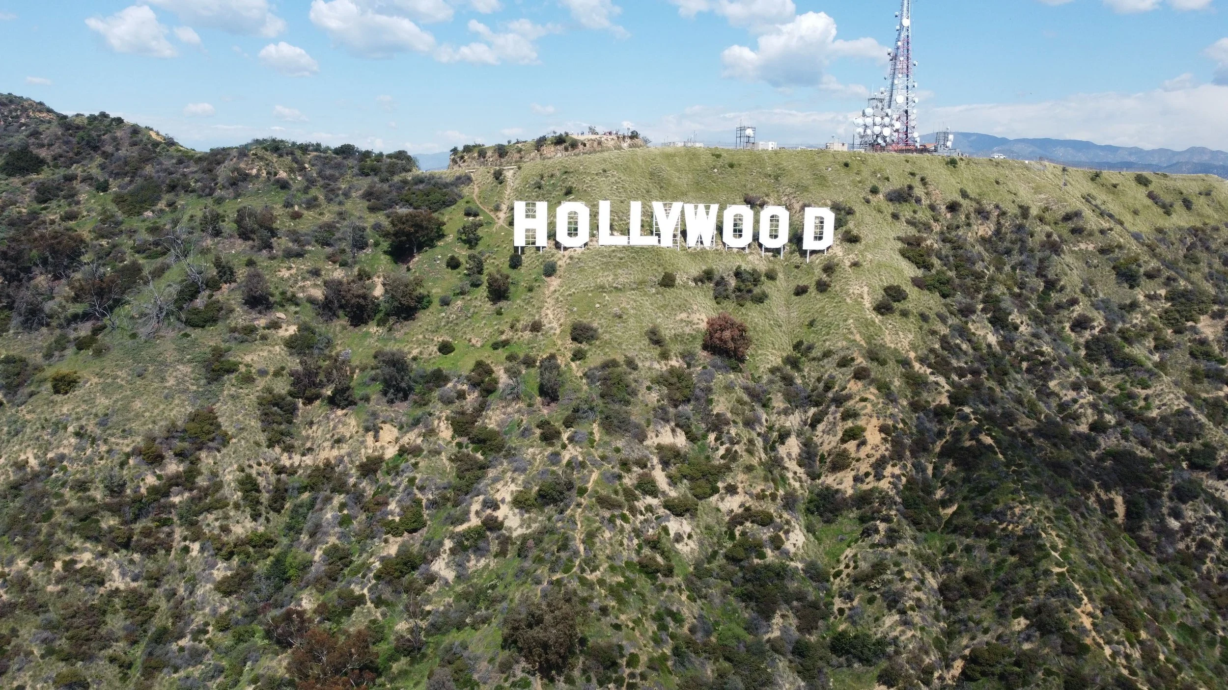 Aerial view of the Hollywood sign on a hillside in Los Angeles, California, with a clear sky and antennas on the hilltop.