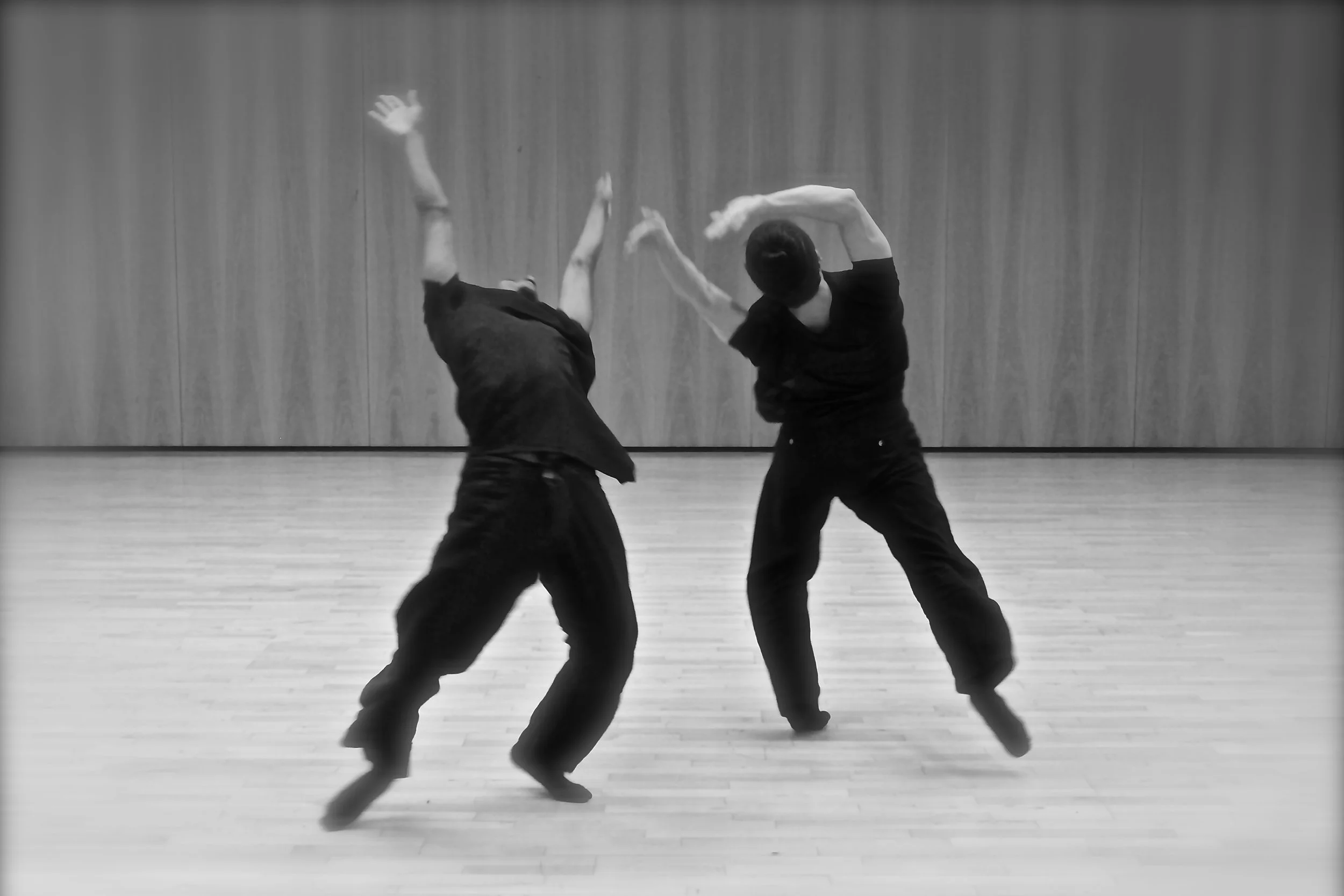 Kenny and Ihsaan dancing in a studio with a wooden floor, captured in black and white. From the choreography Casting Shadows.