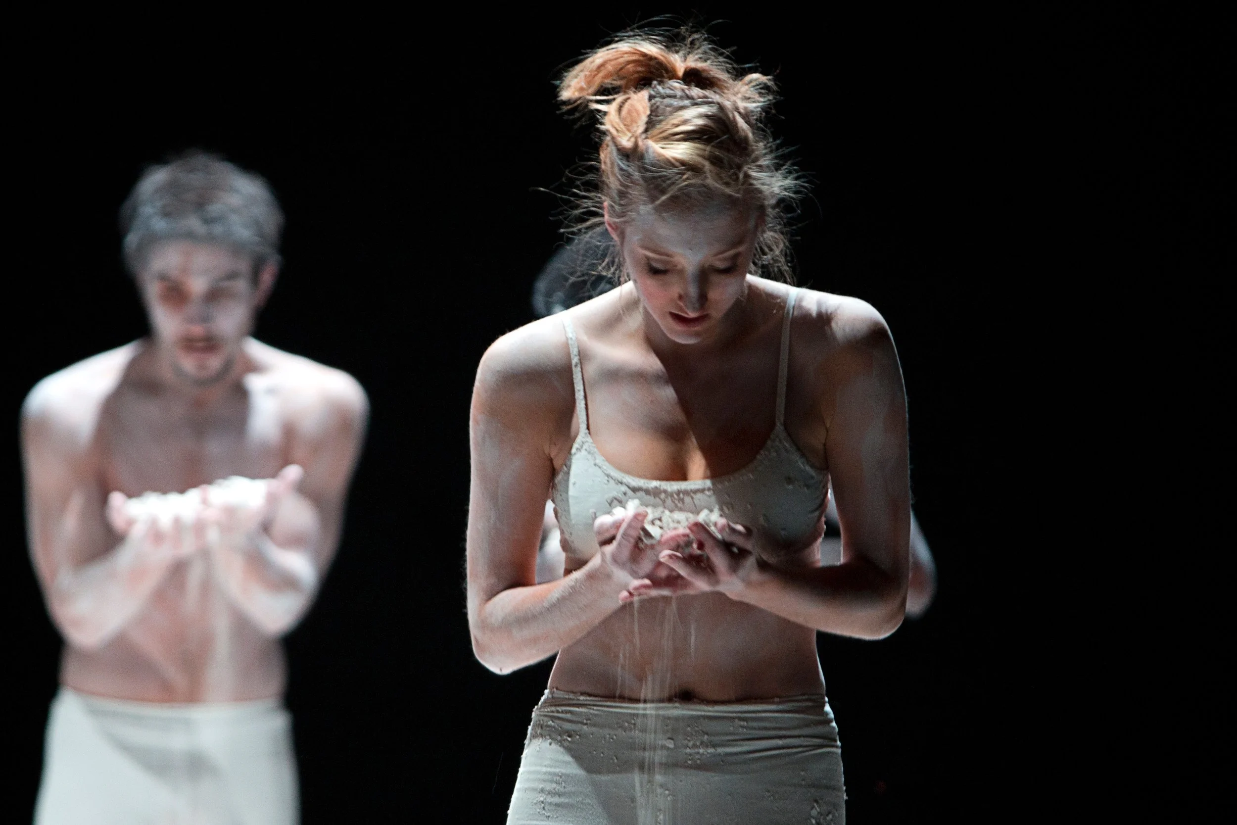 A women and man are covered in white powder or chalk, holding white clay in the dance choreography Dust to Dust.