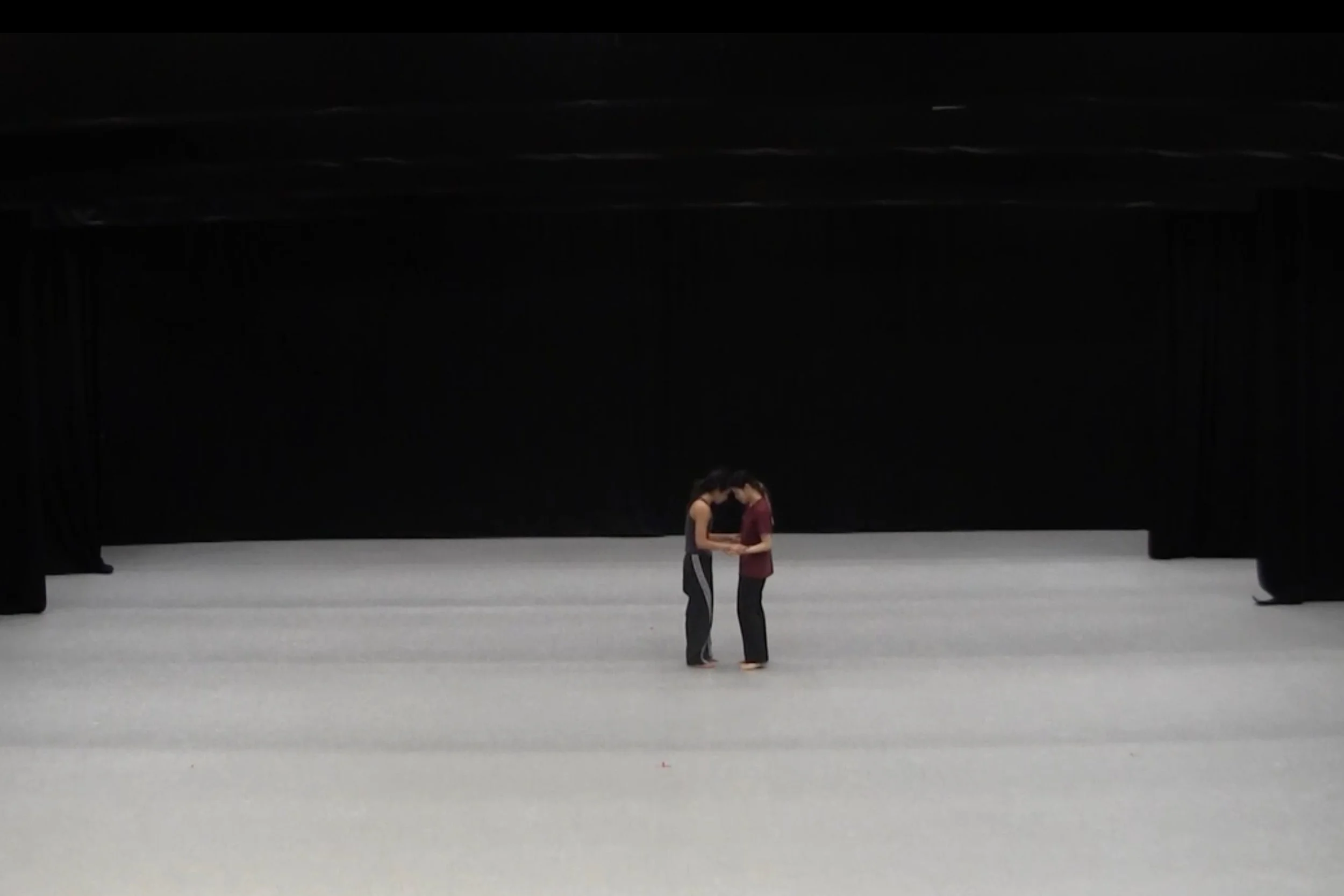Two people standing close together on a large stage with a black curtain backdrop, touching foreheads and holding hands. From the choreography WALLS.