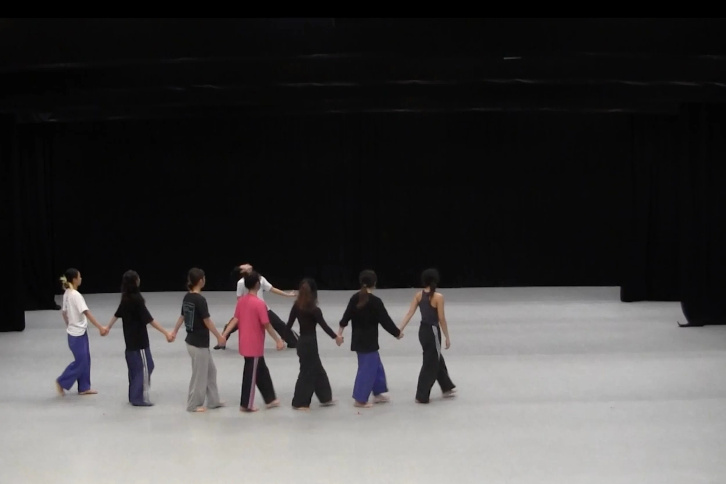 Group of dancer from Hong Kong Academy for Performing Arts holding hands and dancing on stage with a black curtain backdrop. From the choreography WALLS.