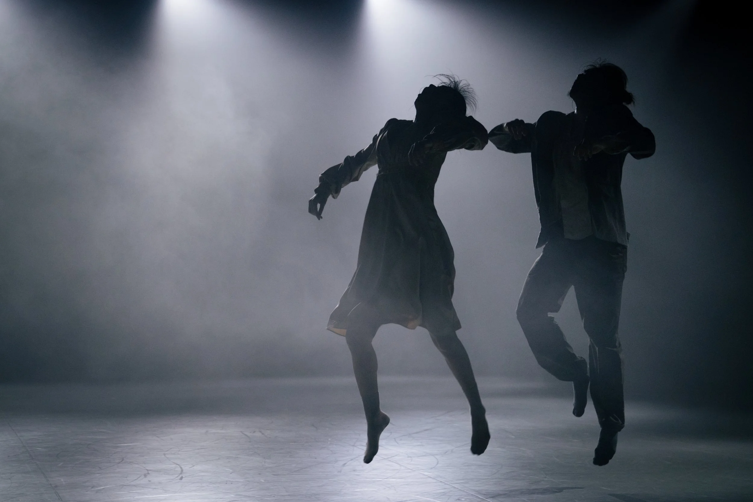 Dancers Yeji and Kenny mid-air on a dimly lit stage in ARRIVAL
