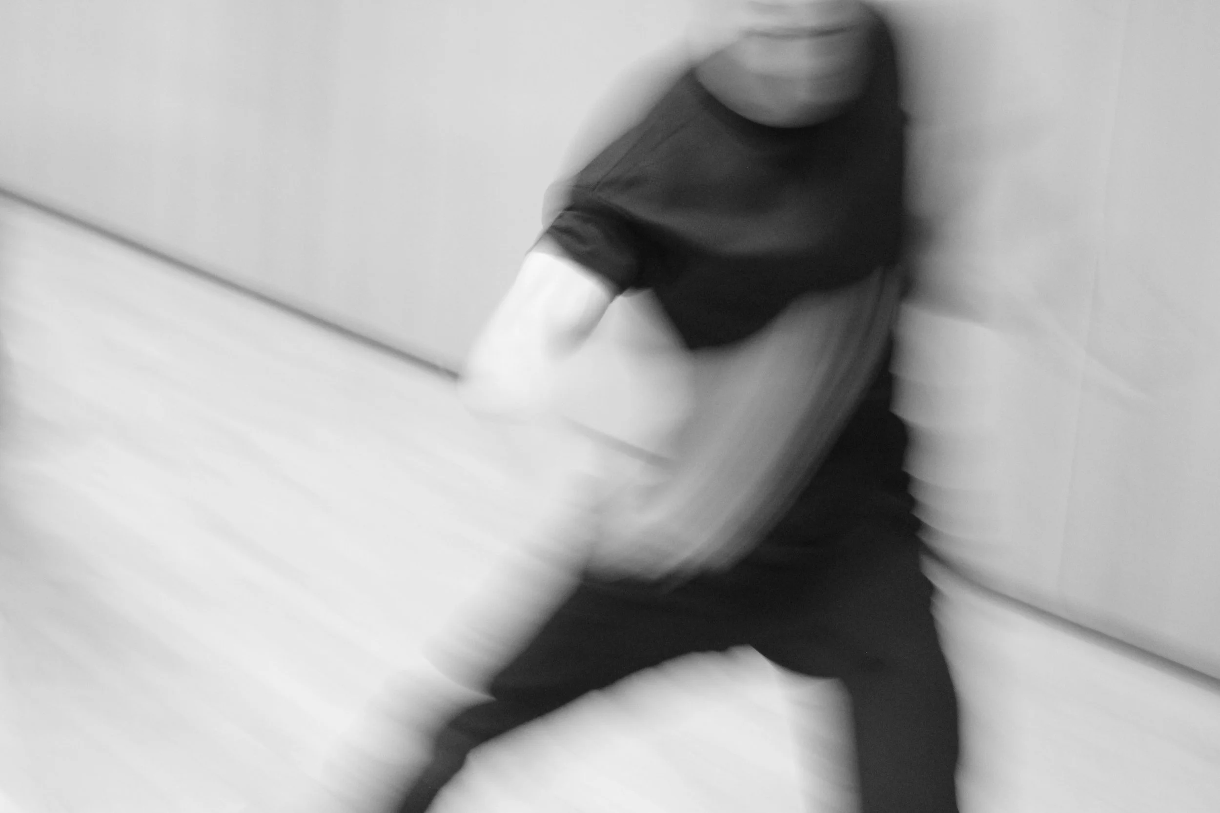 Blurred image of Kenny Ho dancing, wearing a black shirt and dark pants. From the choreography Casting Shadows.