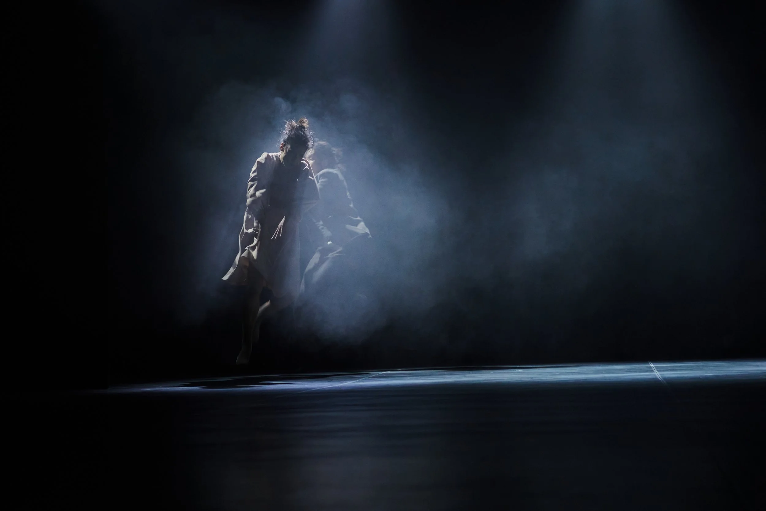 Dancers Yeji and Kenny perform on a dark stage with dramatic lighting, creating a misty atmosphere.