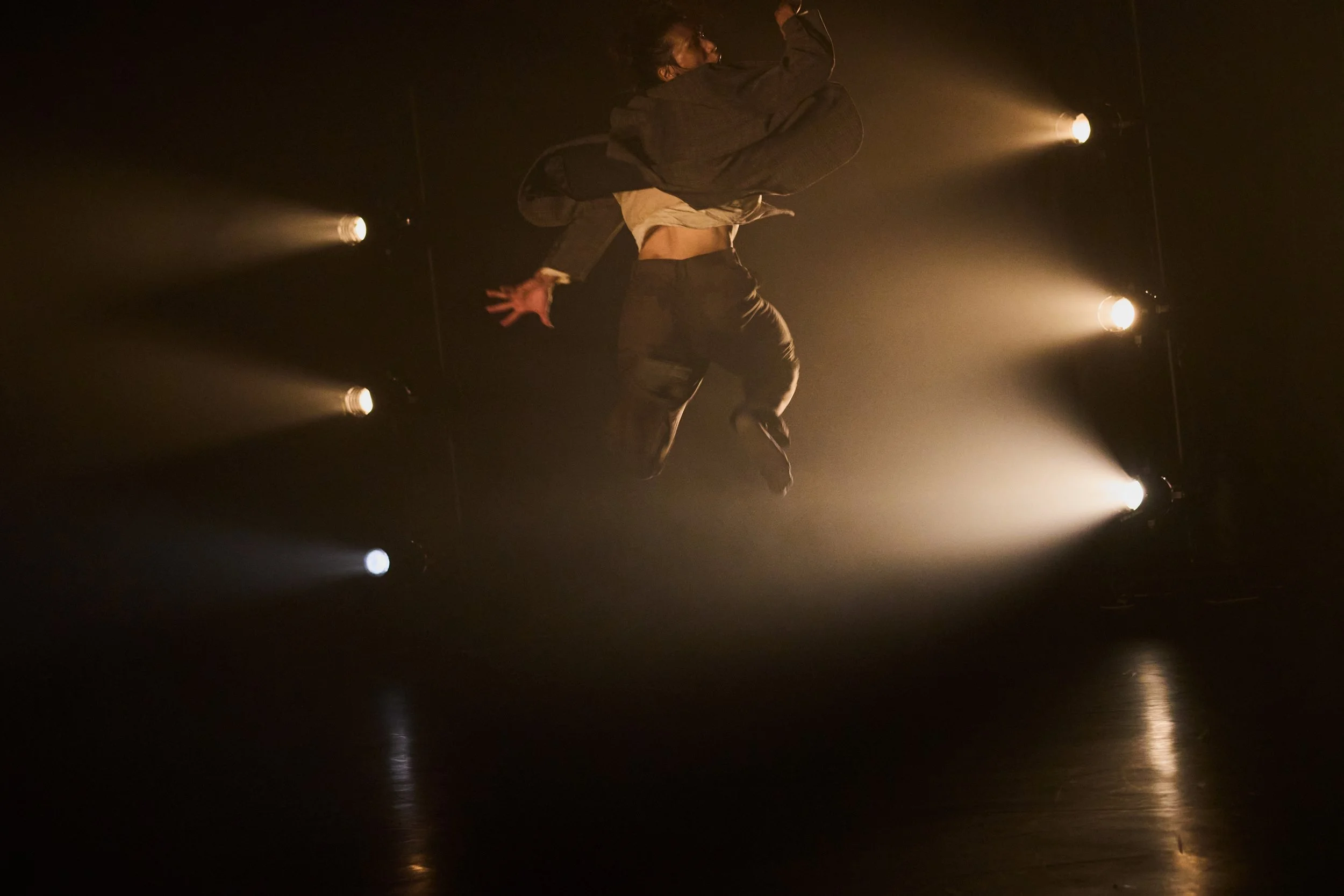 Dancer Kenny Wing Tao Ho performing on stage with dramatic backlighting and smoke or fog effects.