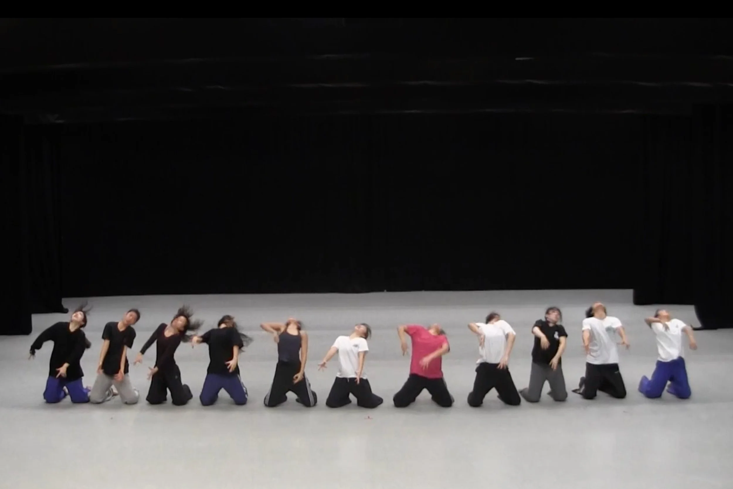 A group of dancers performing on a stage, kneeling and leaning with motions. From the choreography WALLS.
