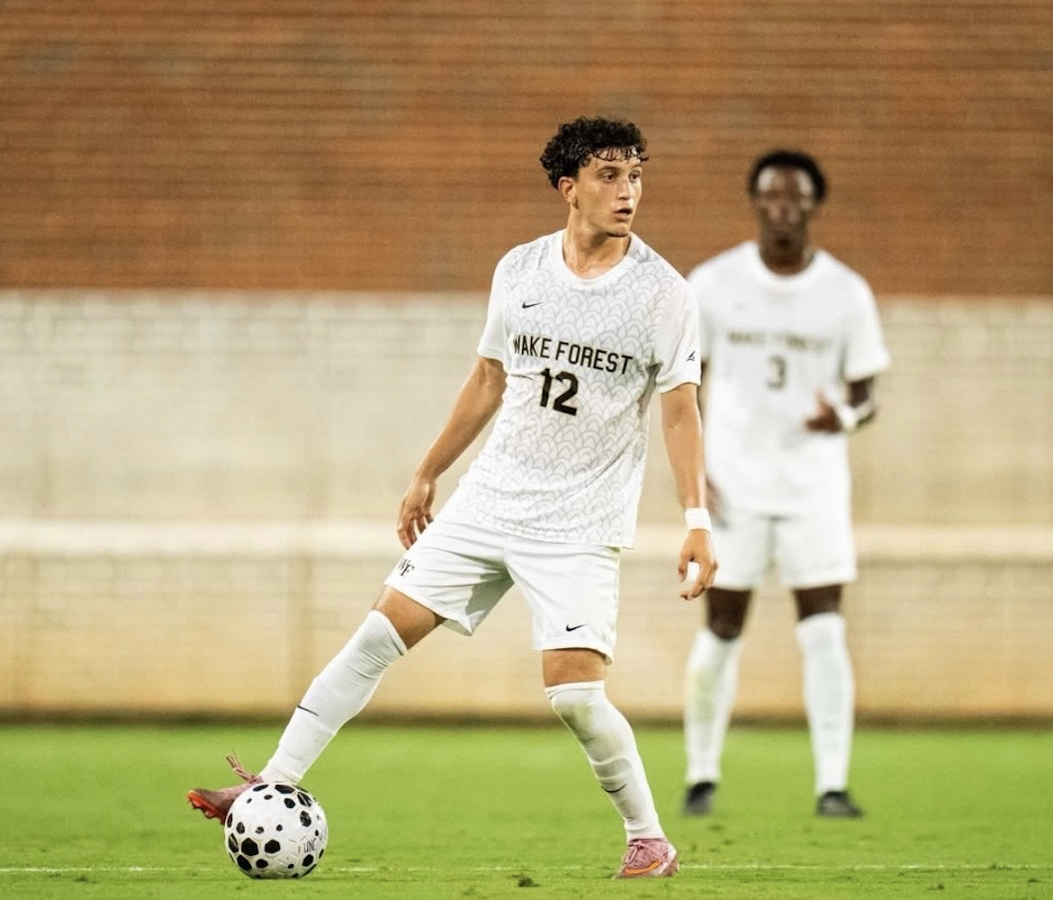 Soccer players in white uniforms on a field, with one player preparing to kick a soccer ball.