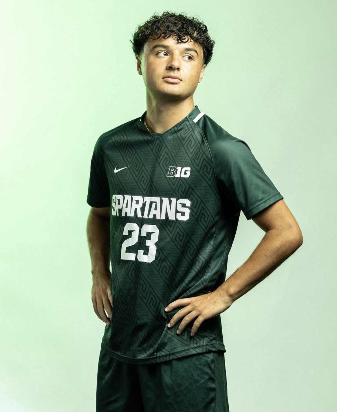 A young man in a dark green Spartans basketball jersey with the number 23 standing against a green background.