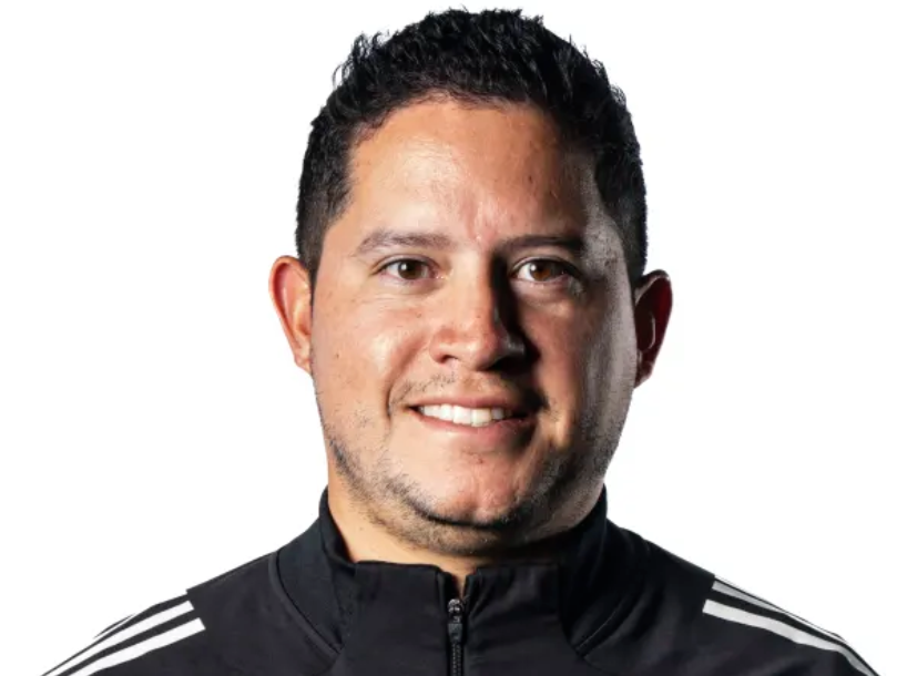 Portrait of a smiling man with short dark hair wearing a black sports jacket with white stripes on the shoulders.