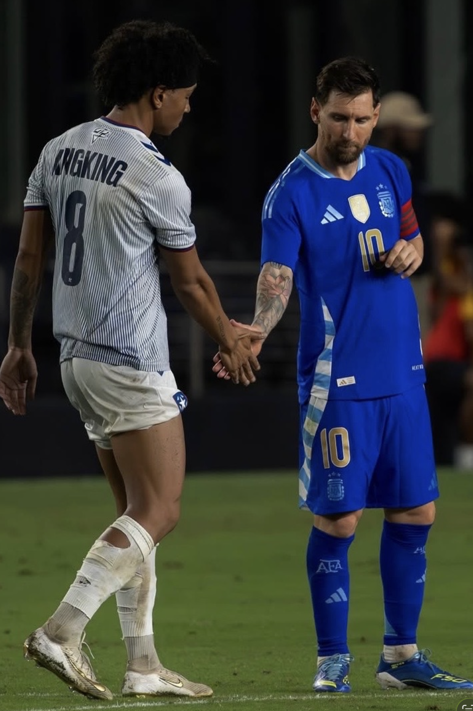 Two soccer players, one from the USA and one from France, holding hands on the field after a match. The French player wears a blue uniform with the number 10, and the American player wears a white uniform with the number 8.