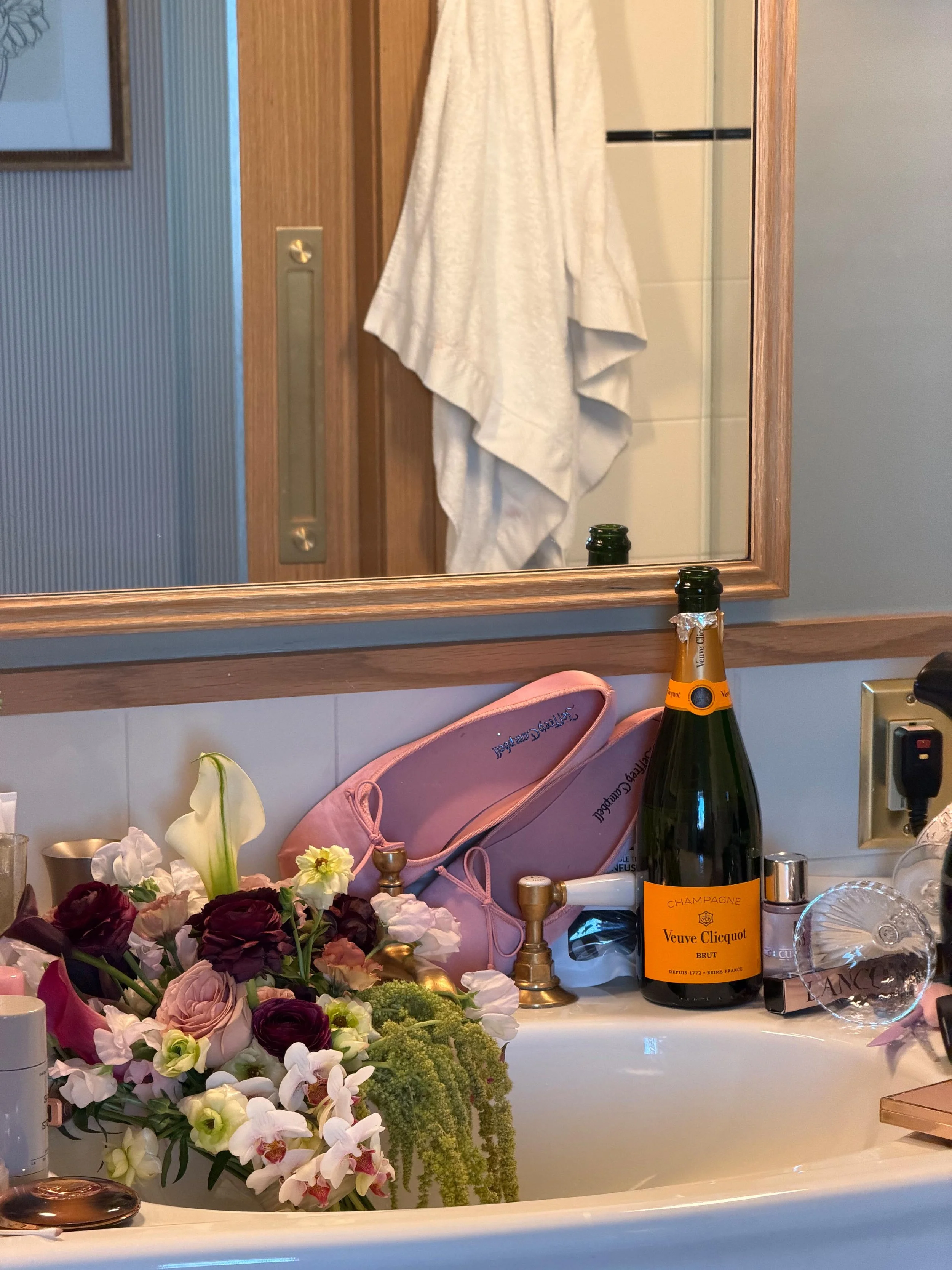 messy bathroom vanity with champagne, bouquet, and ballet flats