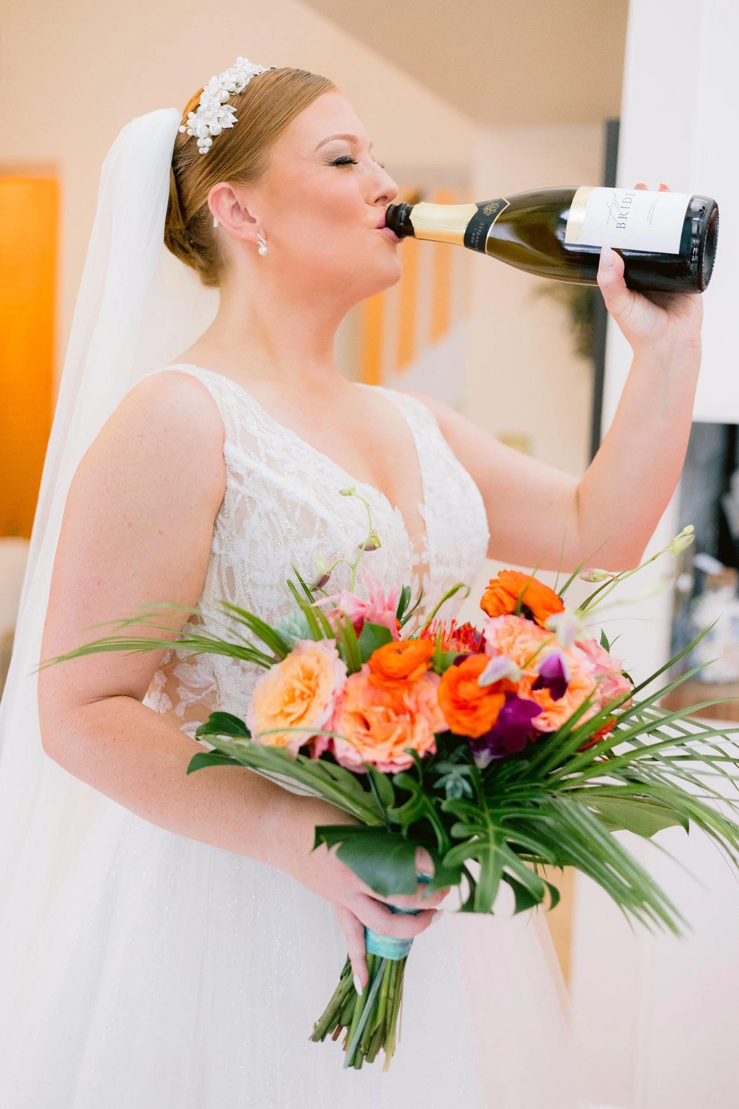 bride holding bouquet in one hand and drinking champagne out of the bottle in the other