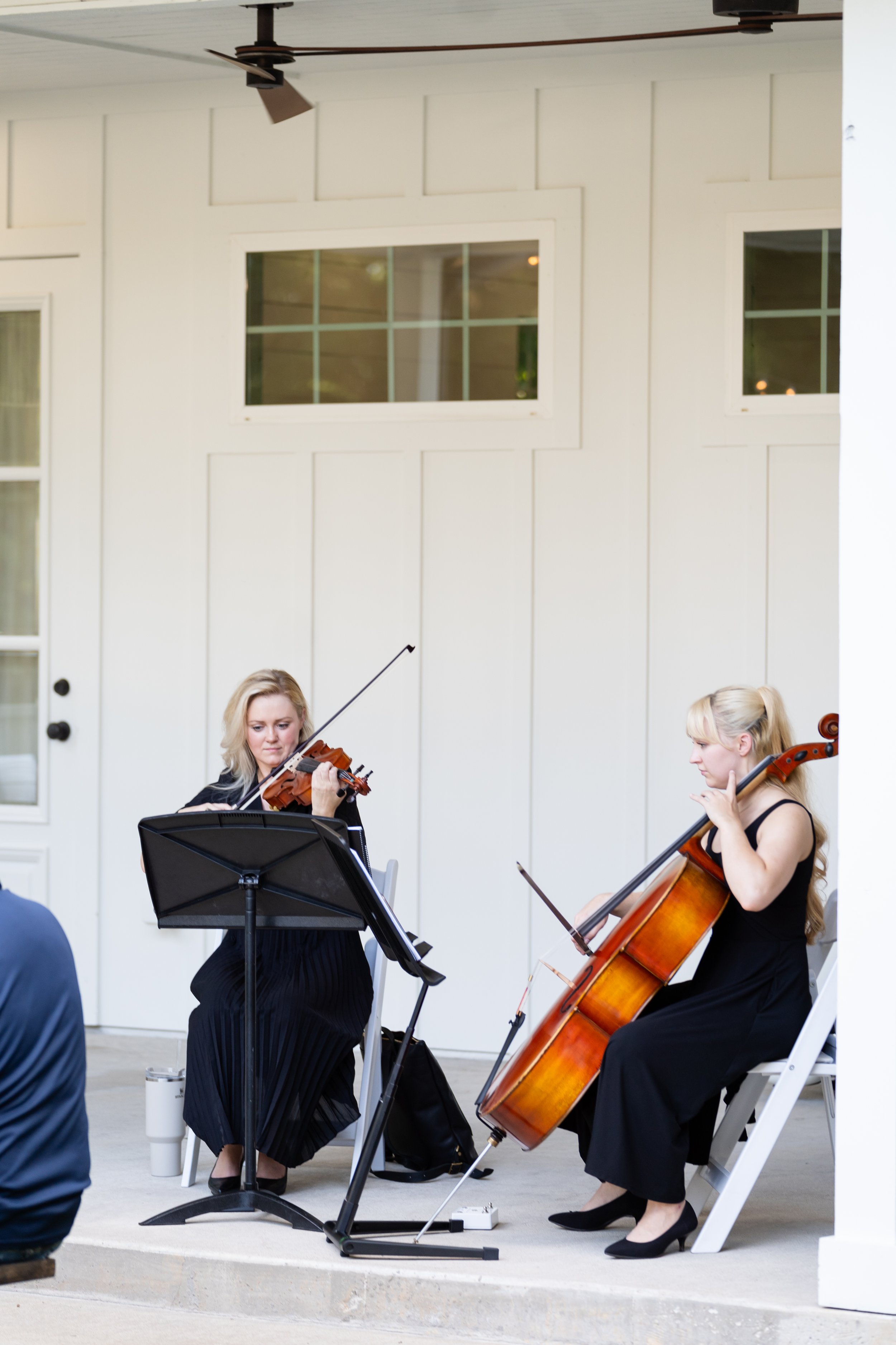 Two women playing string instruments, a violin and a cello, during an outdoor performance.
