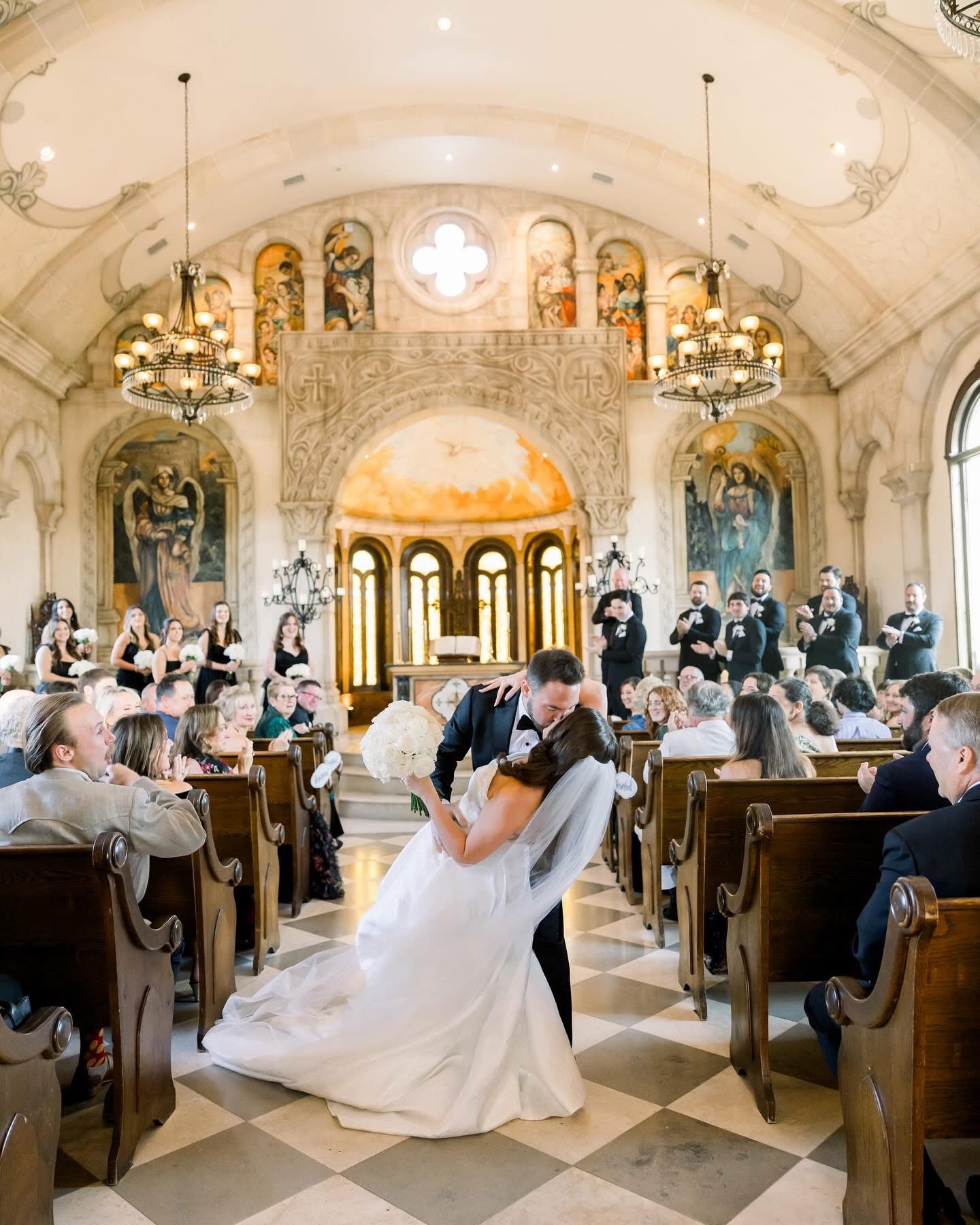 A bride and groom sharing a kiss during their wedding ceremony in a church, with guests seated in pews and a choir standing in the background.