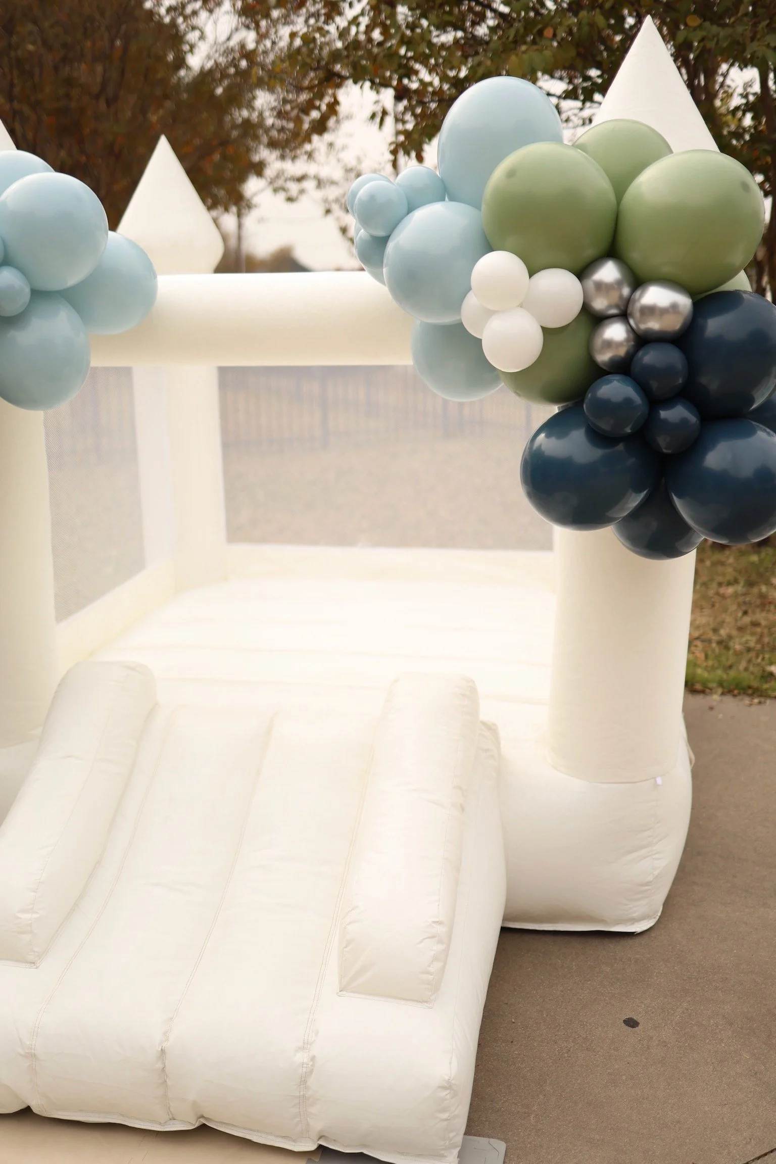 Inflatable white castle with balloon decorations in shades of blue, white, gray, and green, set outdoors.