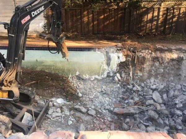 Backhoe excavator breaking concrete during the pool removal process.