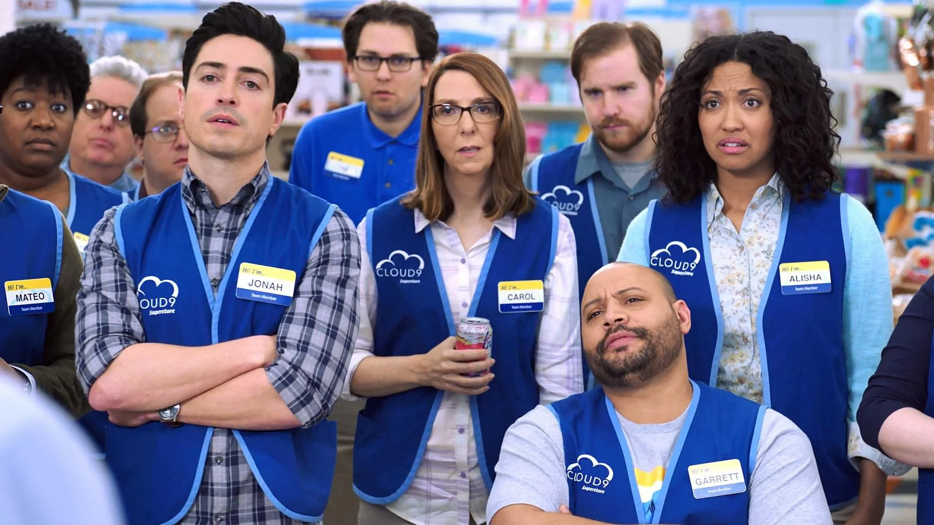 Group of employees wearing blue vests with 'CLOUD9 Superstore' branding, standing in a store aisle, with some looking confused or surprised.