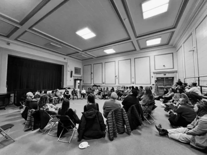 Group of people sitting in a circle in a large room attending a PTA meeting.