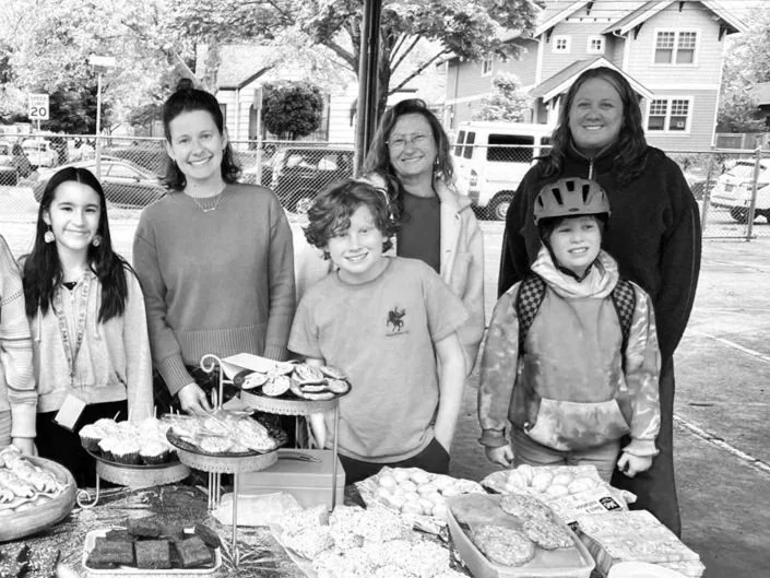 Group of five smiling students and parents posing at the fifth grade fundraiser bake sale.