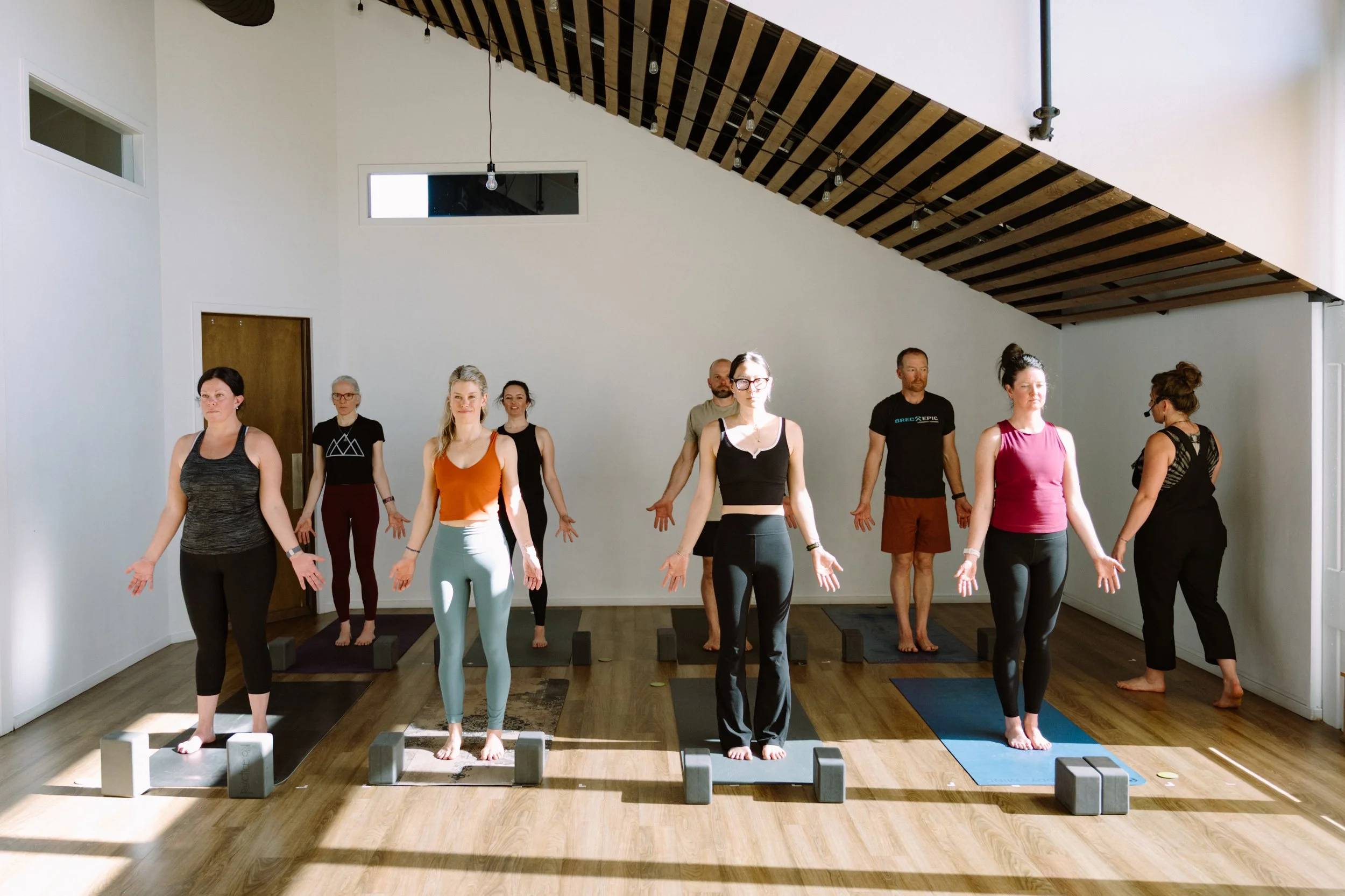 Group of people practicing yoga or meditation in a well-lit indoor studio with minimalist design and wooden ceiling.