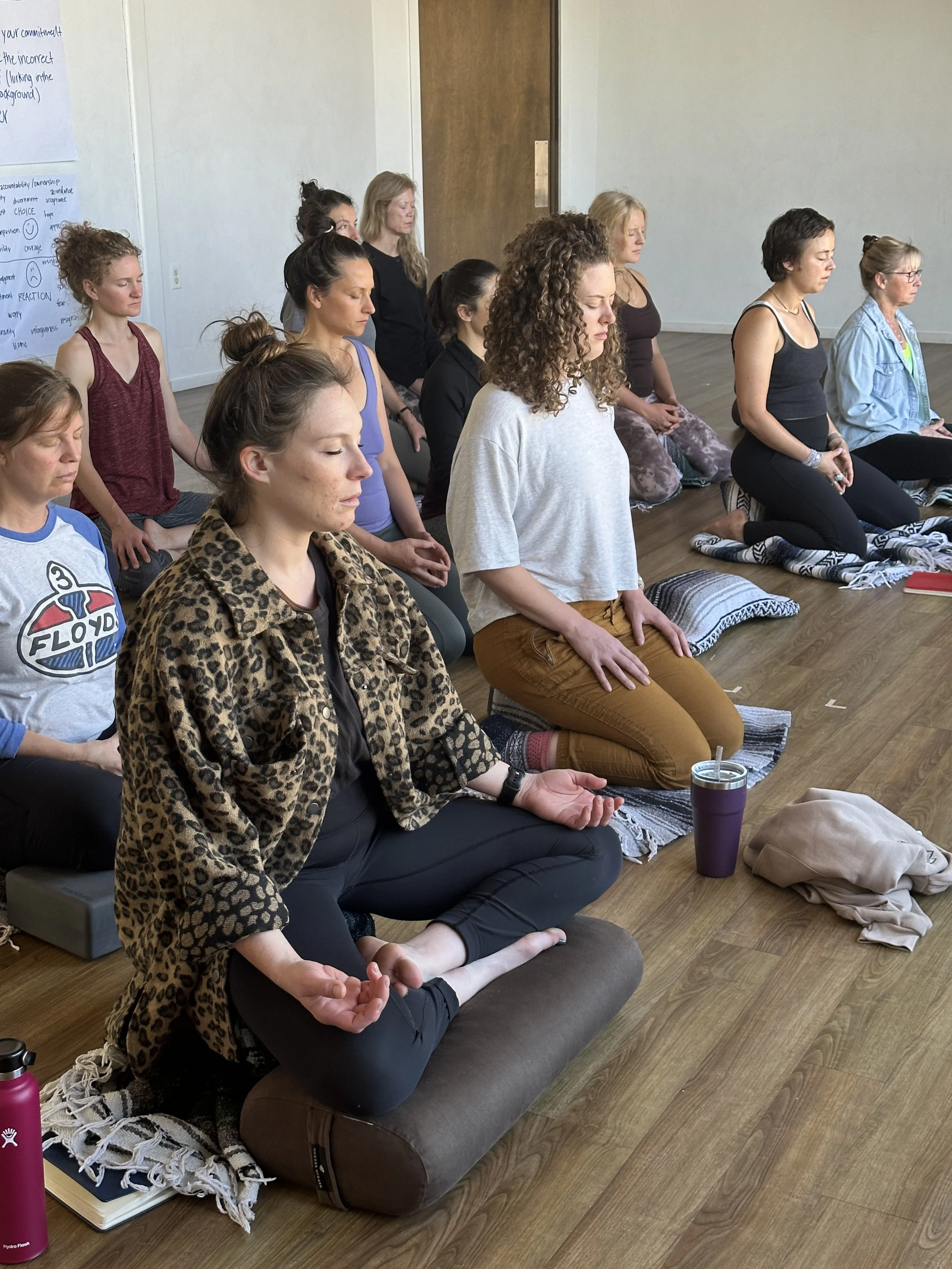 Group of women meditating, sitting on cushions with eyes closed and hands resting on their laps.