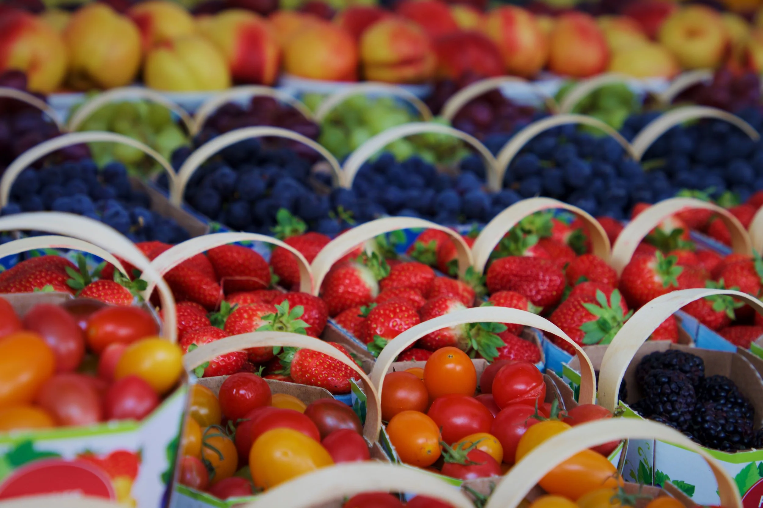 A display of baskets filled with fresh strawberries, blueberries, blackberries, raspberries, and small yellow and orange tomatoes at a market.
